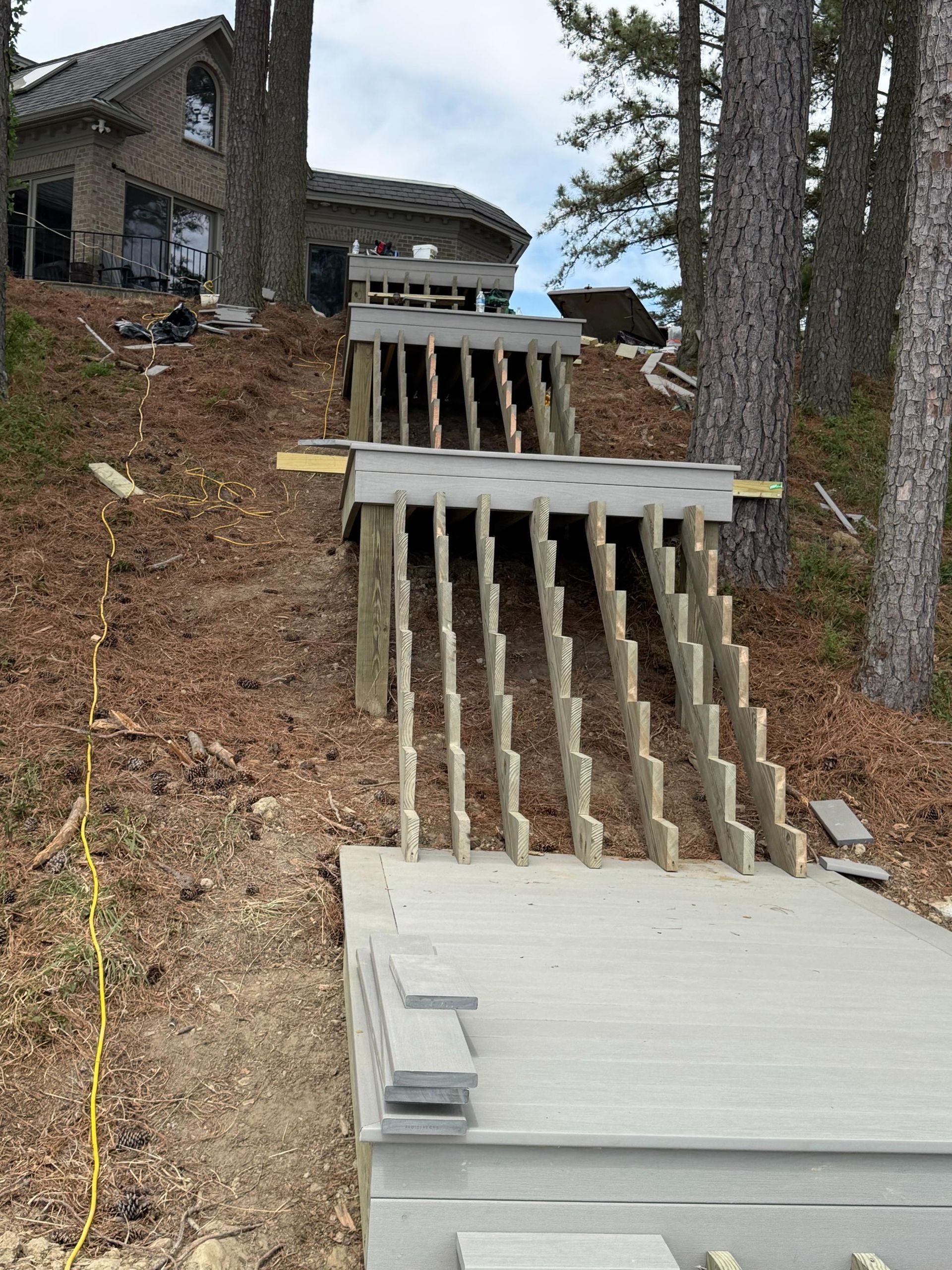 Steep hillside with damaged wooden stairs and retaining wall beside a house, covered in dirt and trees