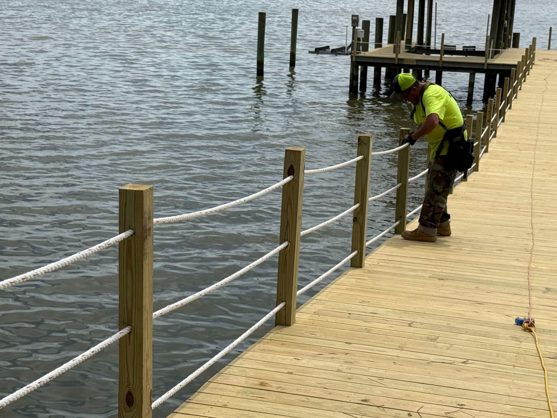 Worker in a neon safety vest inspecting a wooden dock by the water.
