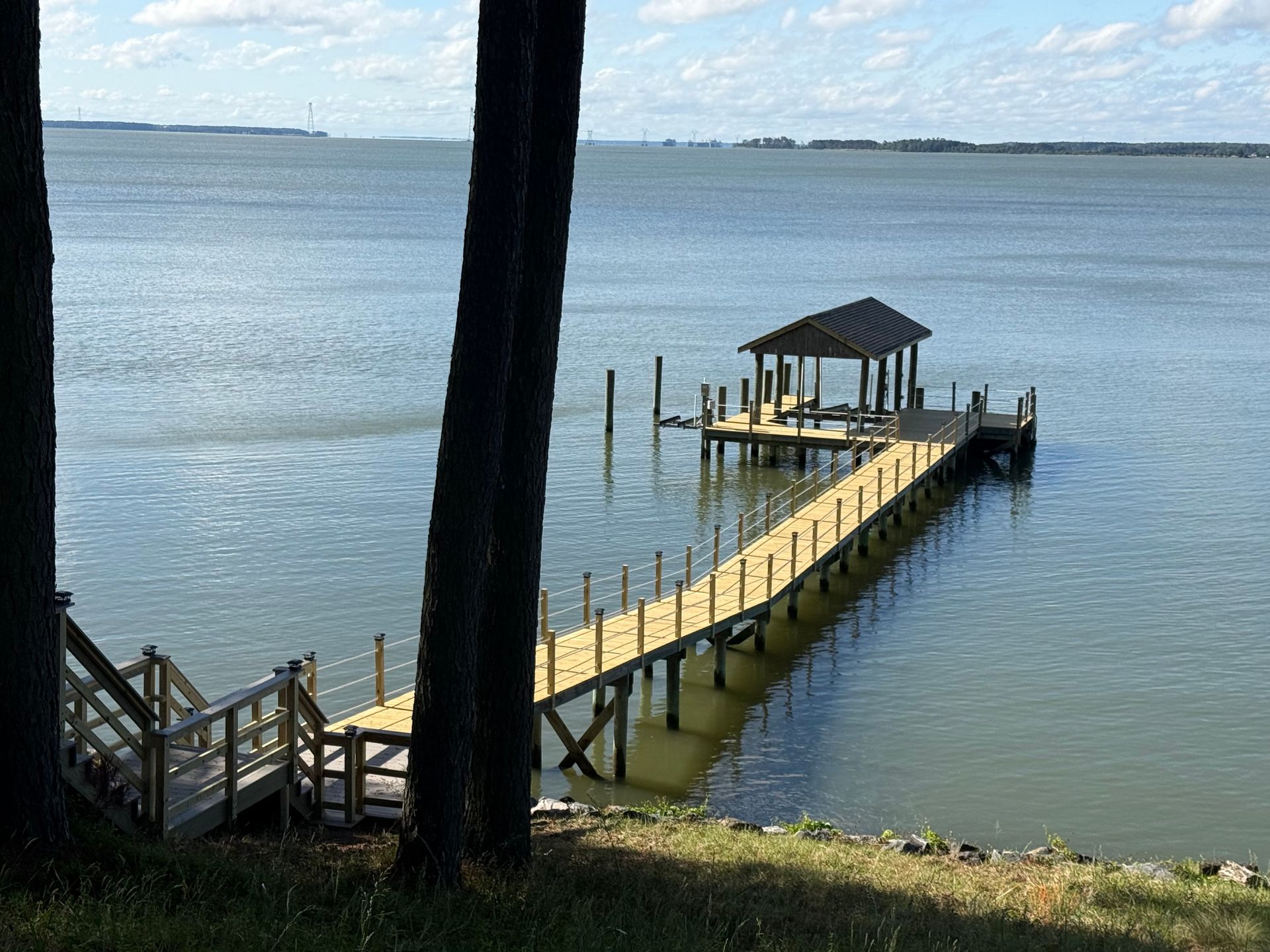 Wooden dock with gazebo extending into a calm blue bay on a sunny day