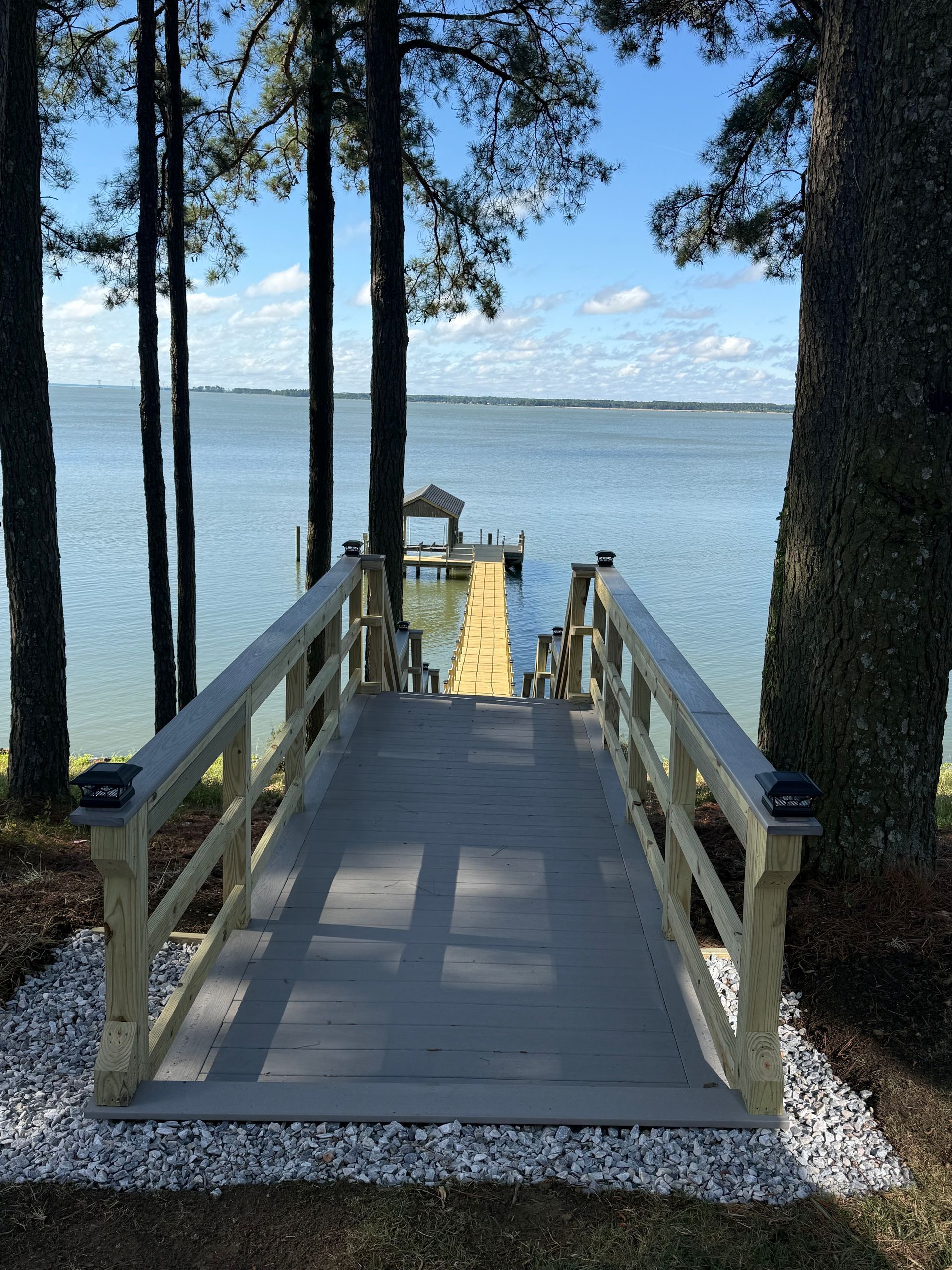 Wooden dock walkway through trees leading to a calm lake under a blue sky