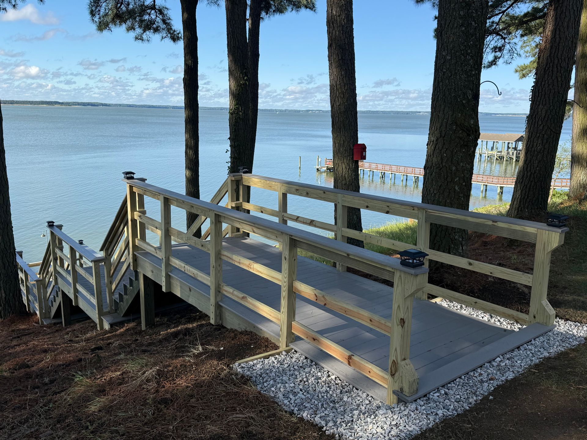 Wooden ramp and stairs leading to a dock over a calm lake, with trees and railings along the shore.