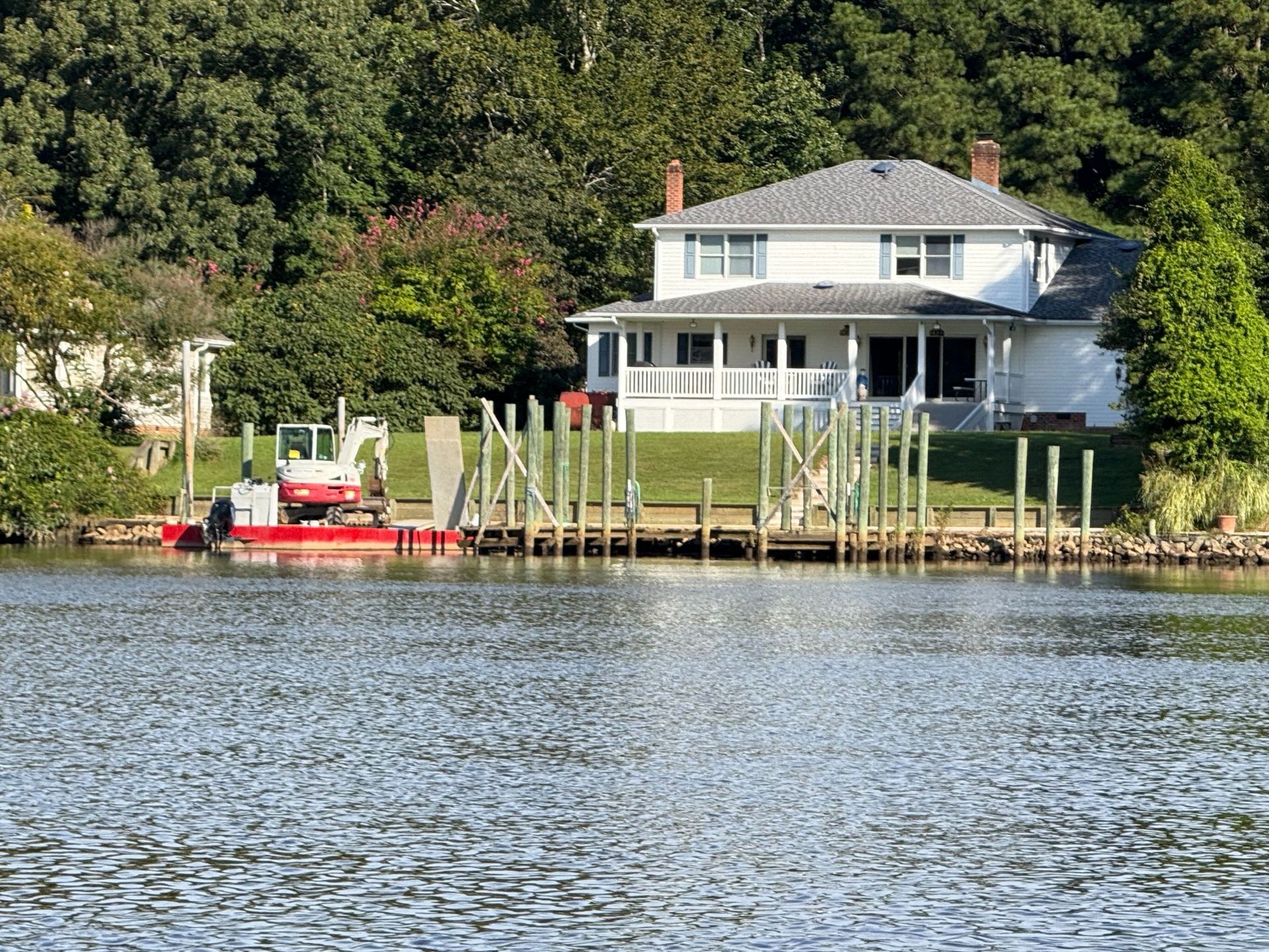 White house with porch by a body of water; dock in foreground, trees behind.