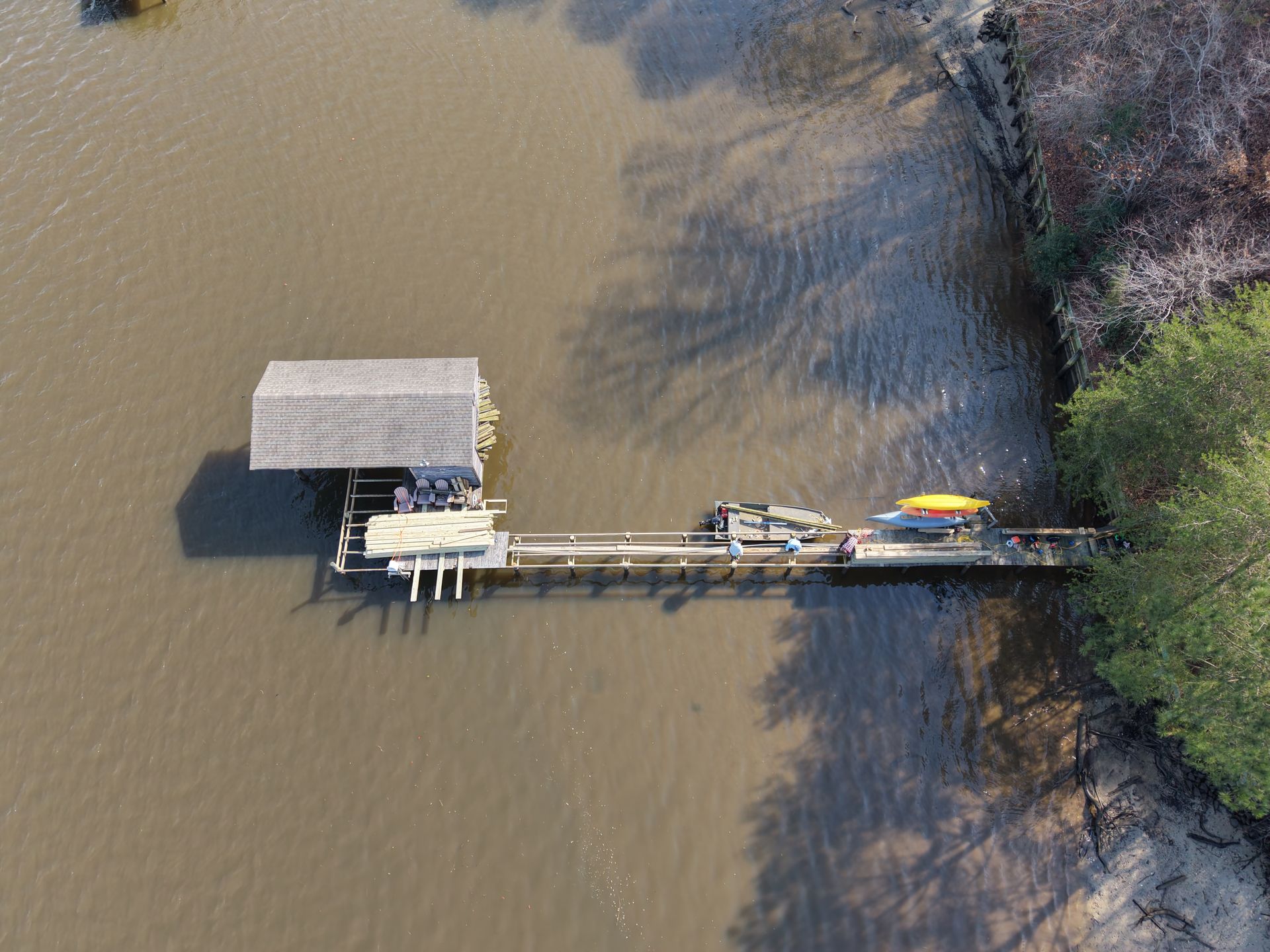 Aerial view of a wooden dock and boathouse on muddy water, with small boats moored along the pier.