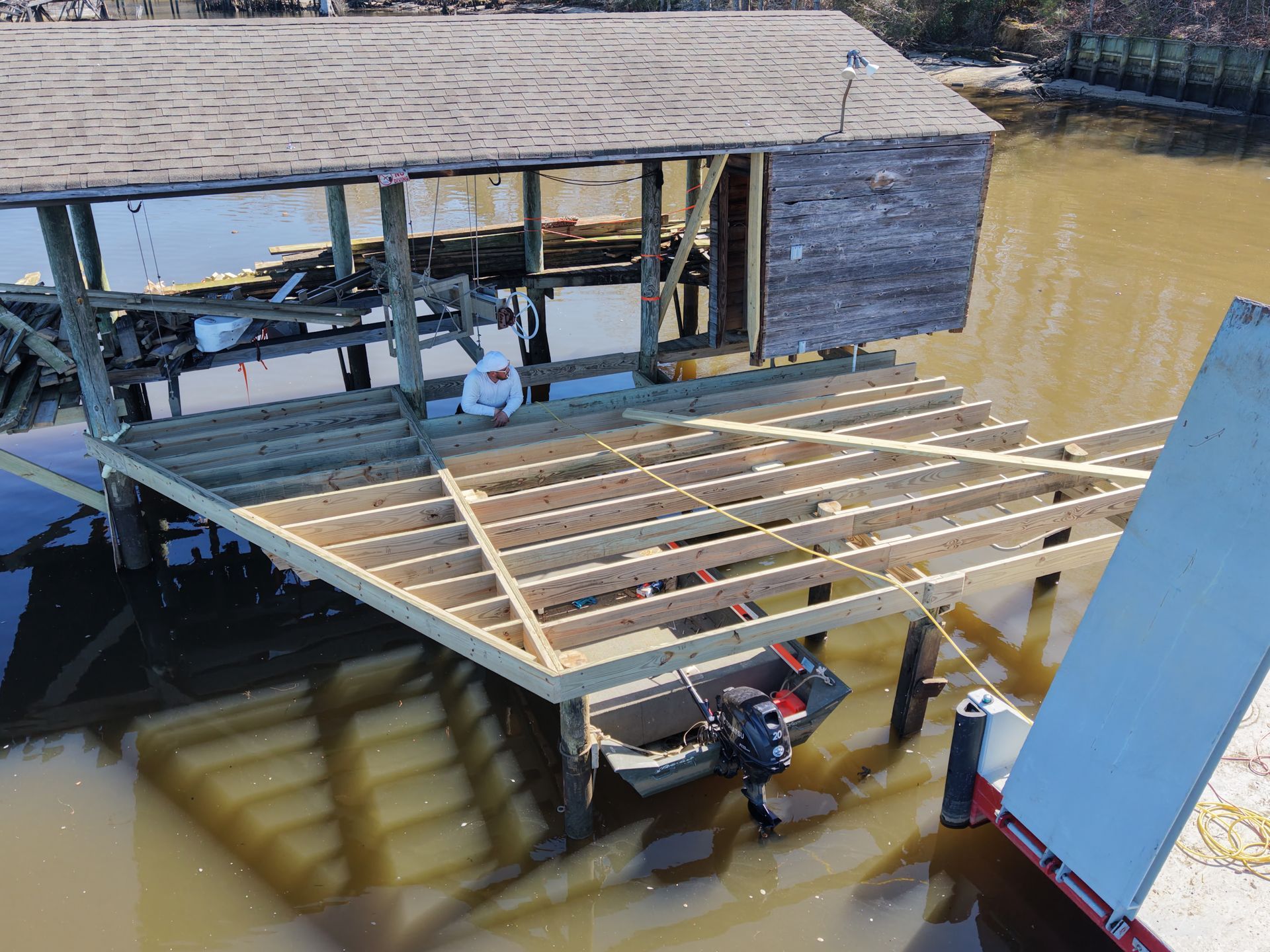 Floating dock frame under construction beside muddy water, with tools and a small boat underneath