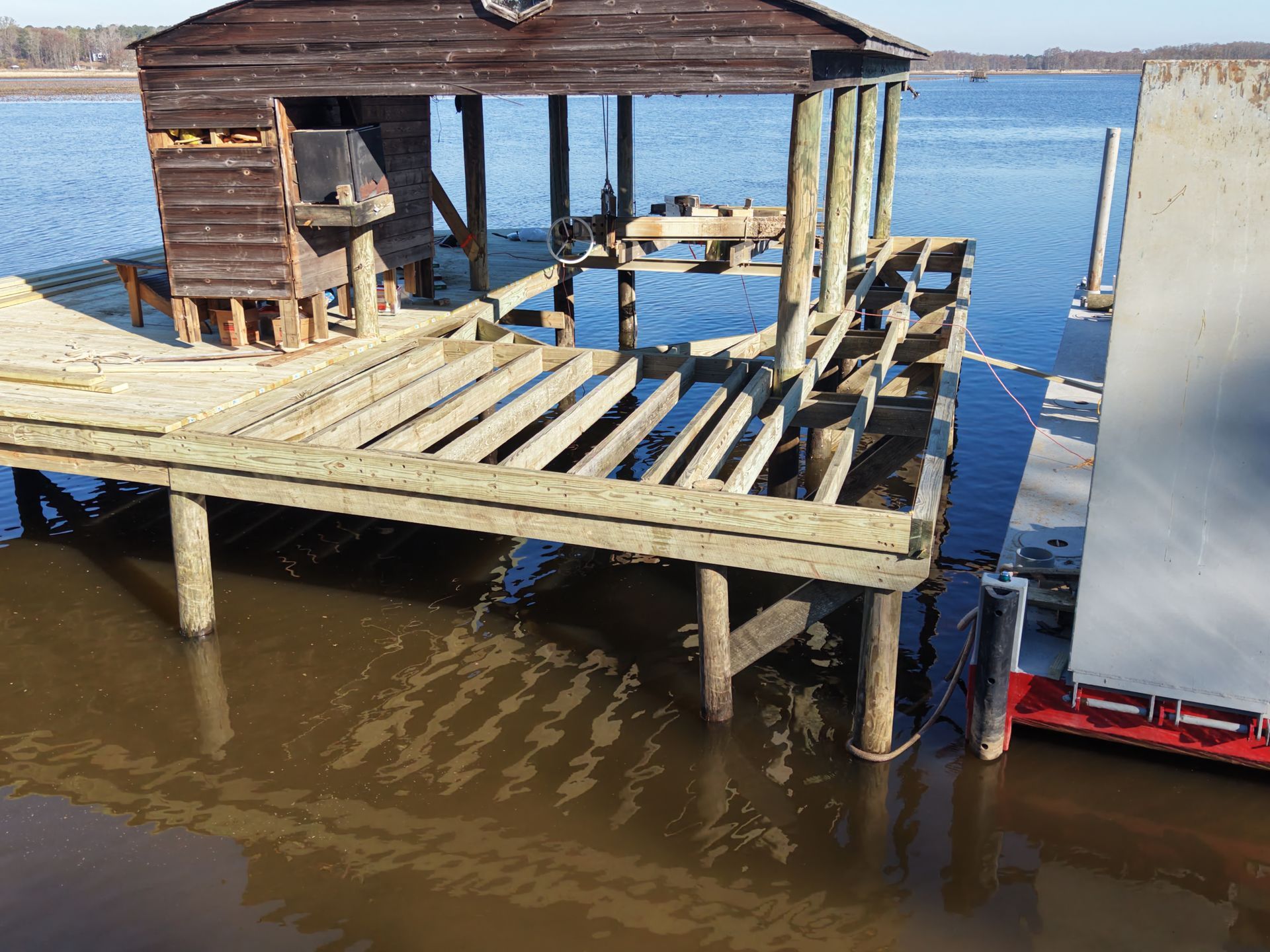 Weathered wooden dock and small shed on stilts over muddy water beside a boat.