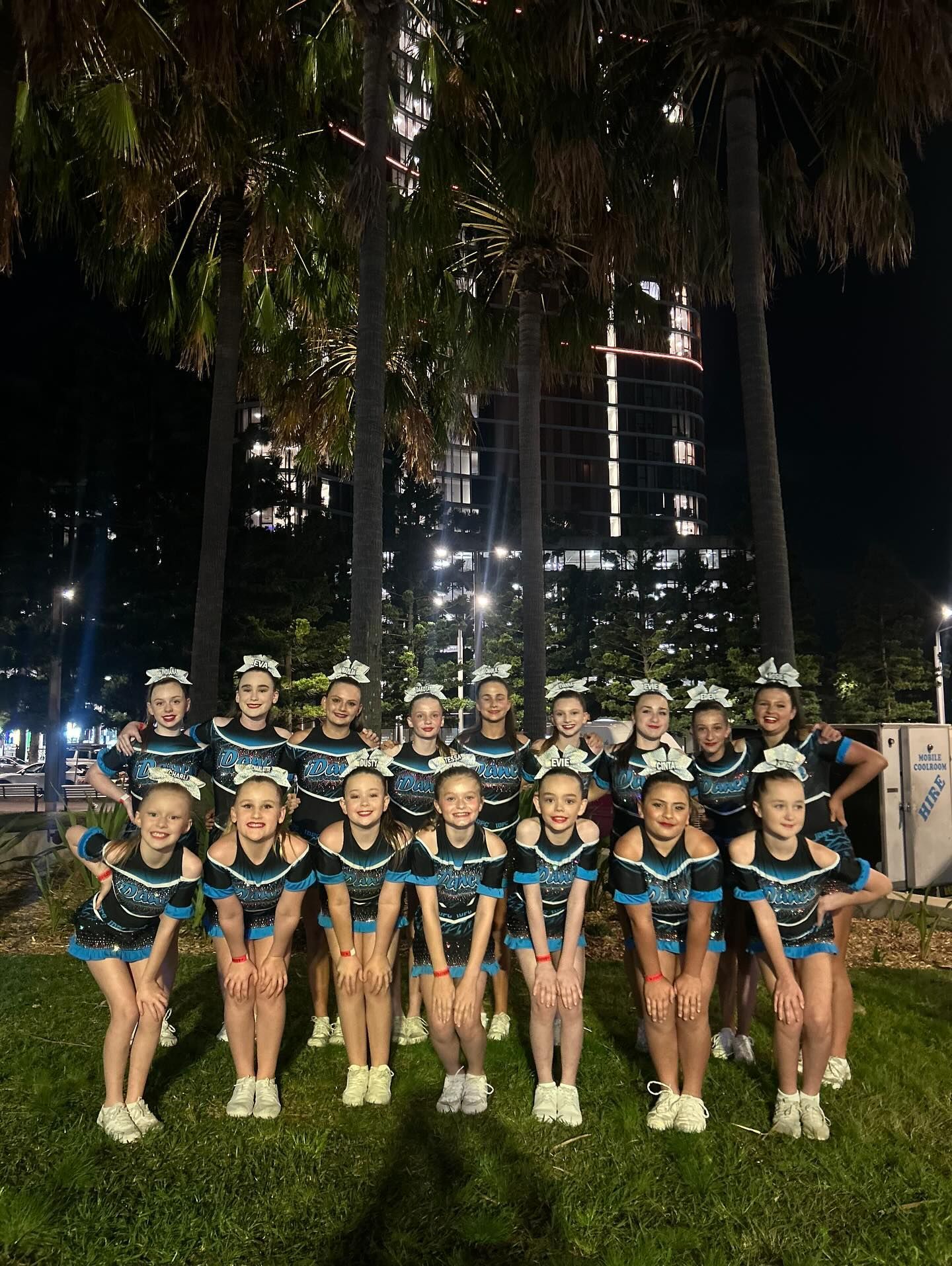 Cheerleading Team in Black and Teal Uniforms Posing on Grass at Night — iDance Performance Co In Medowie, NSW
