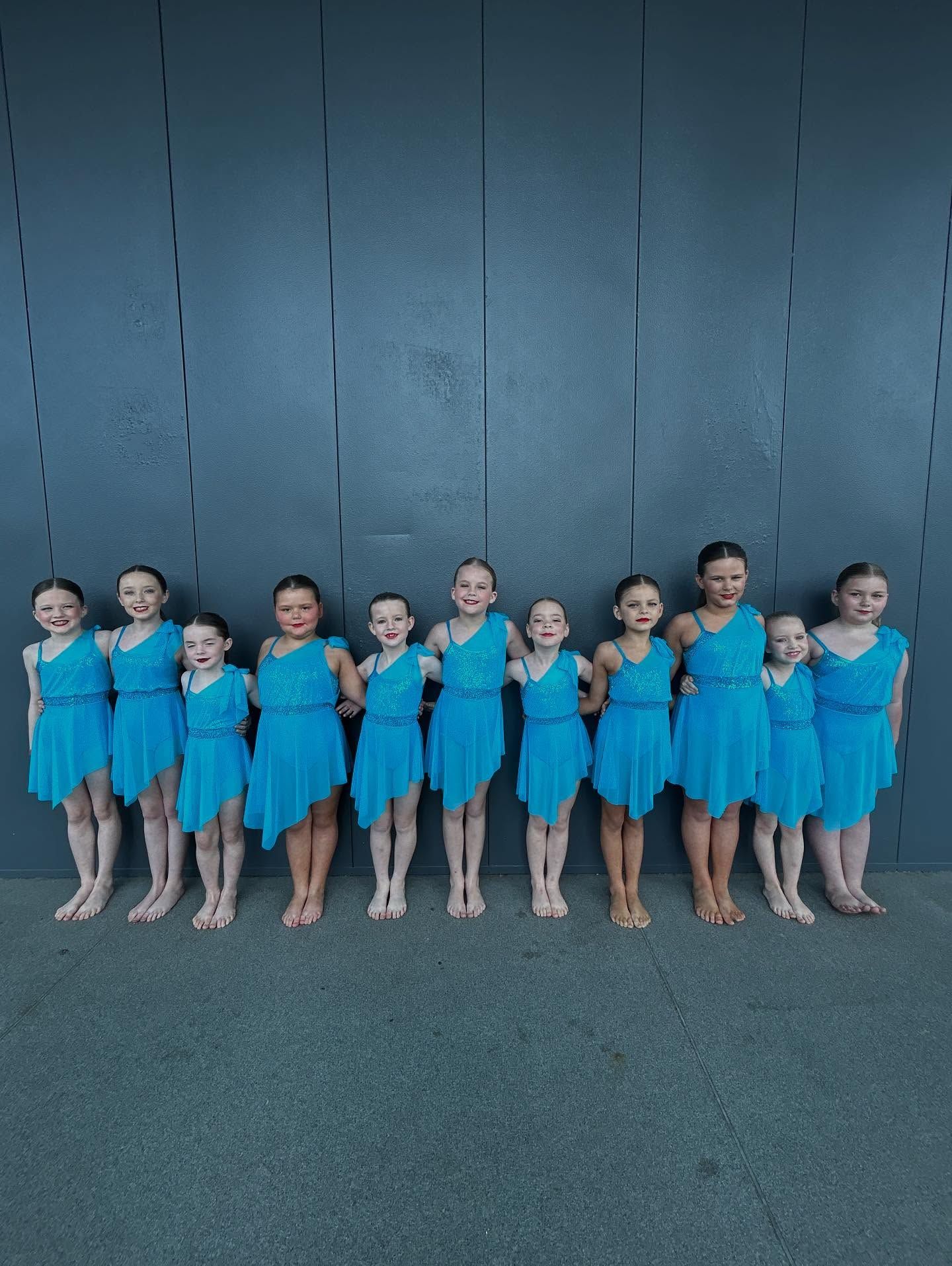 A Dance Group of Eleven Children in Teal Dresses, Posed in Front of a Blue Wall — iDance Performance Co In Medowie, NSW