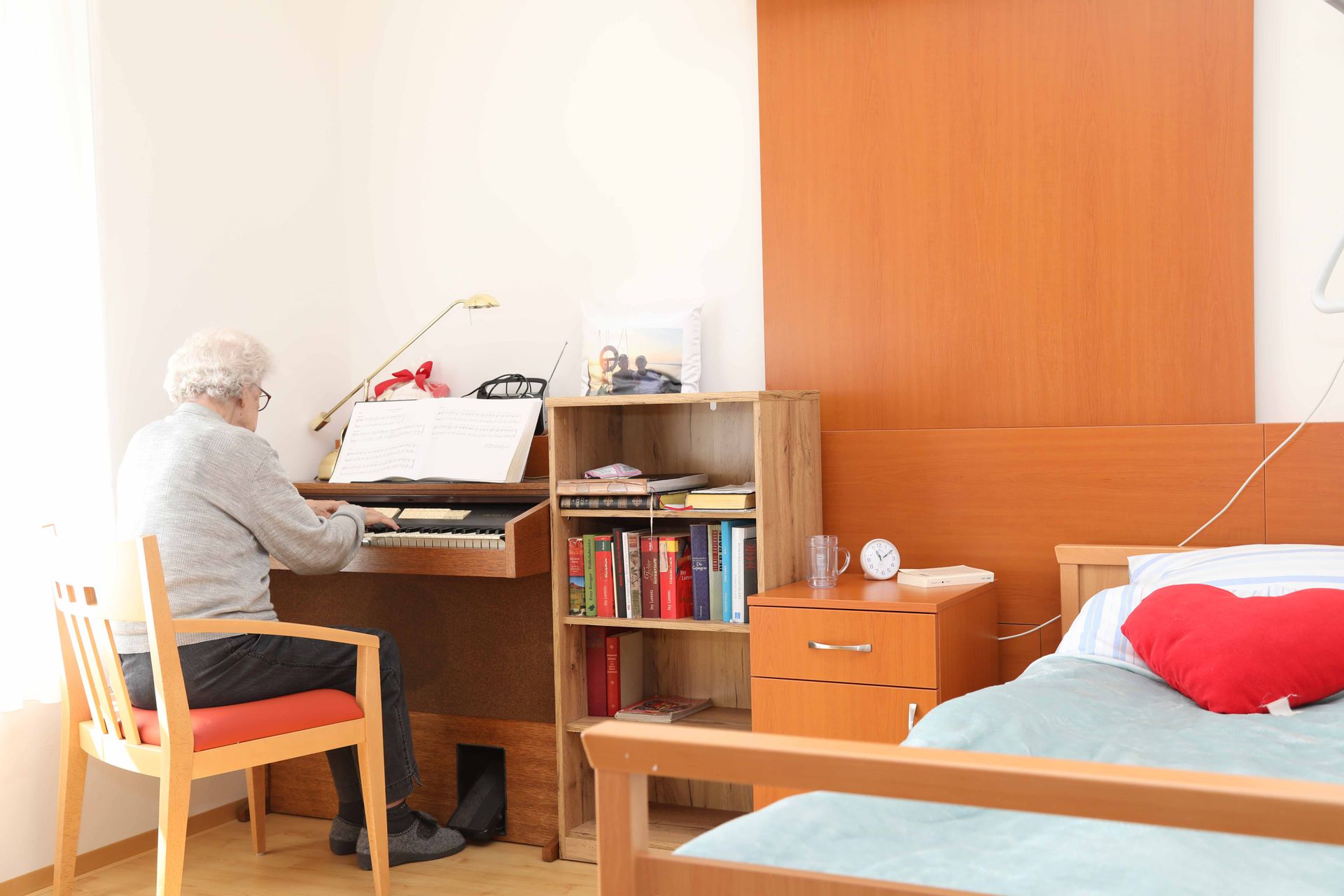 Ein älterer Mann sitzt an einem Schreibtisch in einem Schlafzimmer.