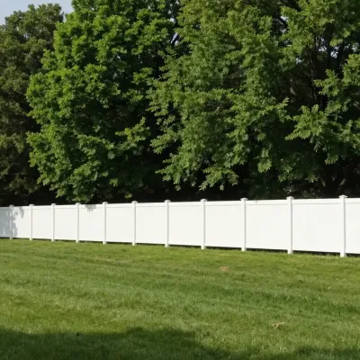 White vinyl fence on a grassy hill, with green trees in the background.