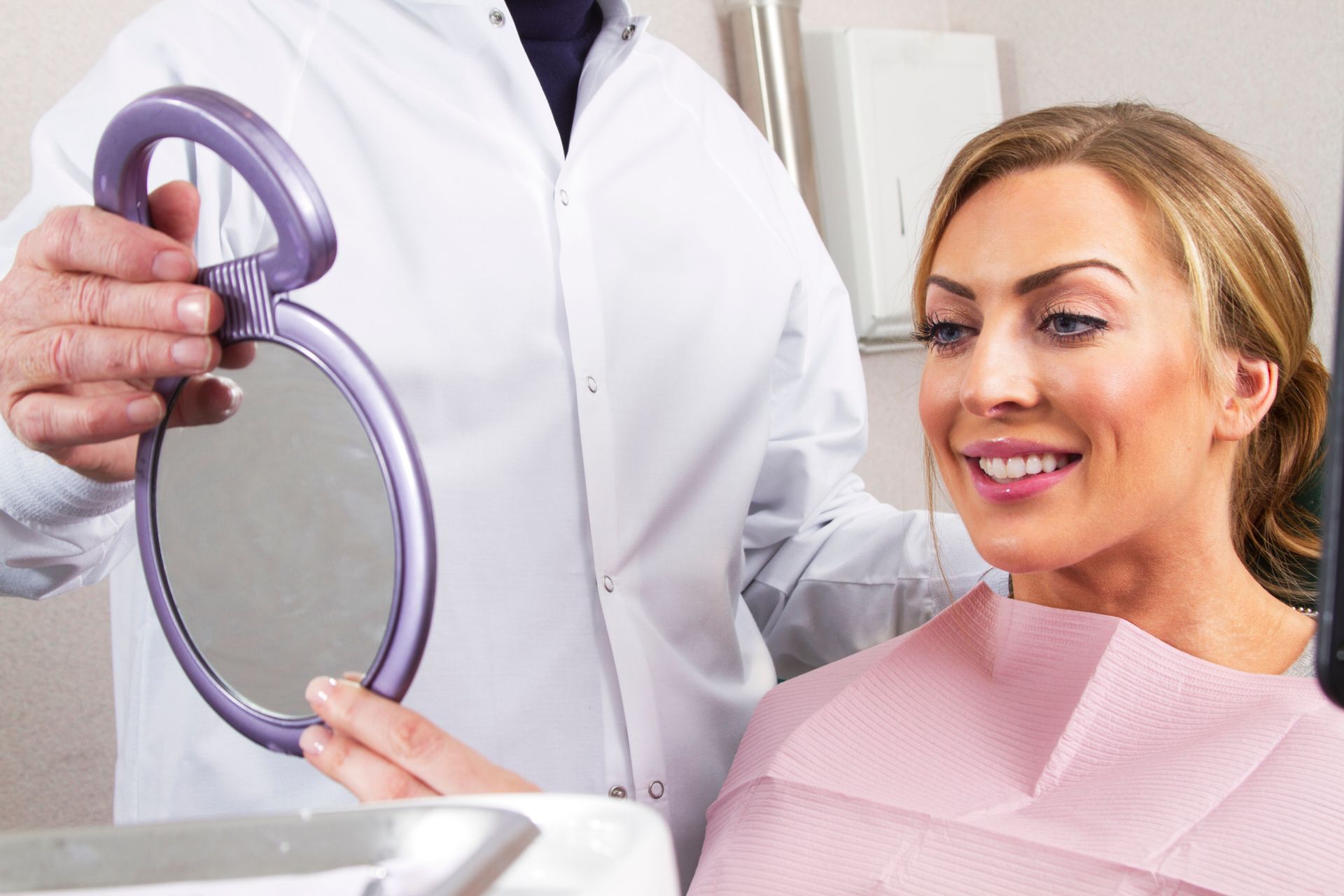 A dentist holds a handheld mirror so his patient can see her smile. A dentist holds a handheld mirror so his patient can see her smile.