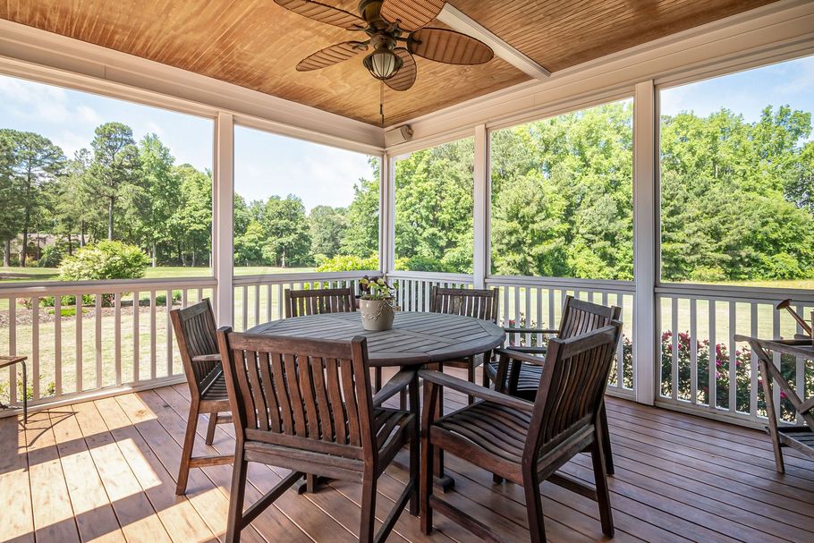 Covered wooden deck with round table and chairs overlooking a green yard