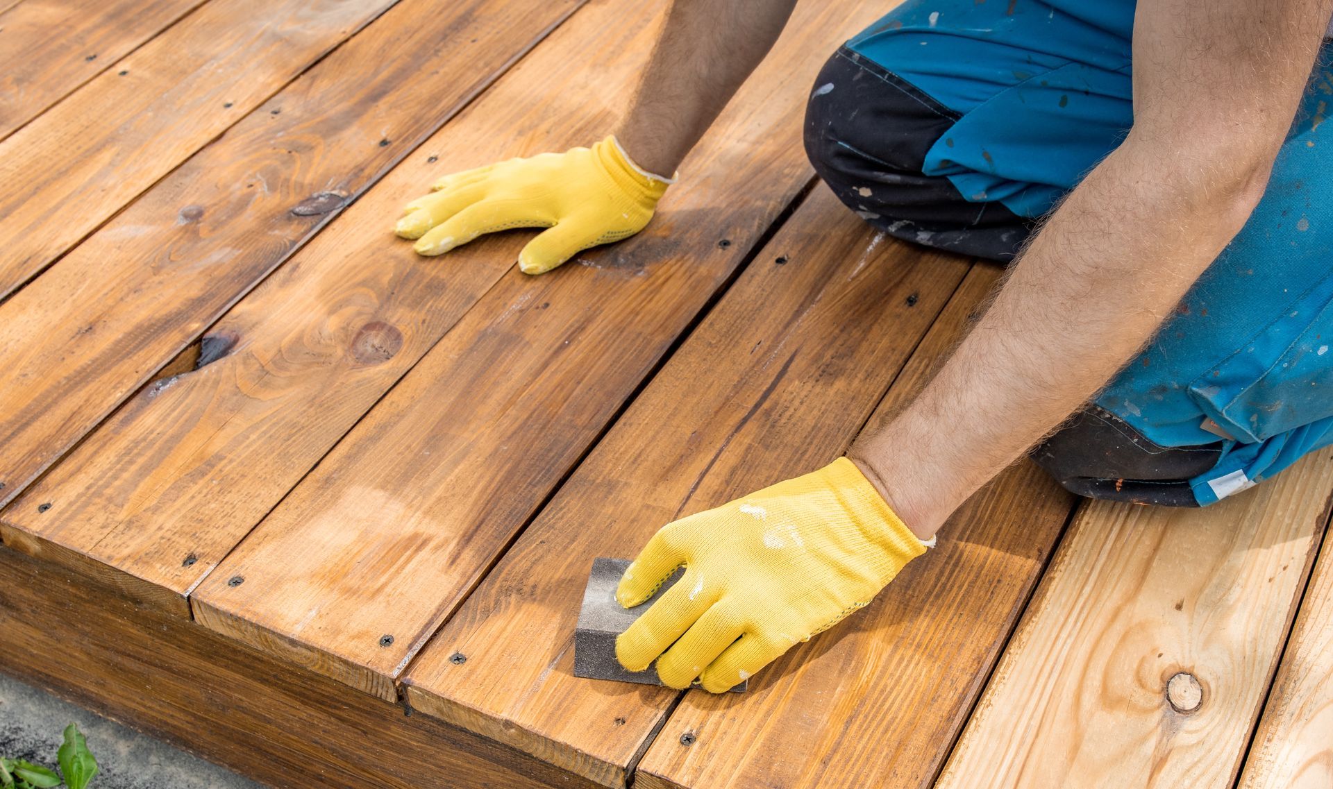 Person in yellow gloves installing wooden deck boards with a power drill.