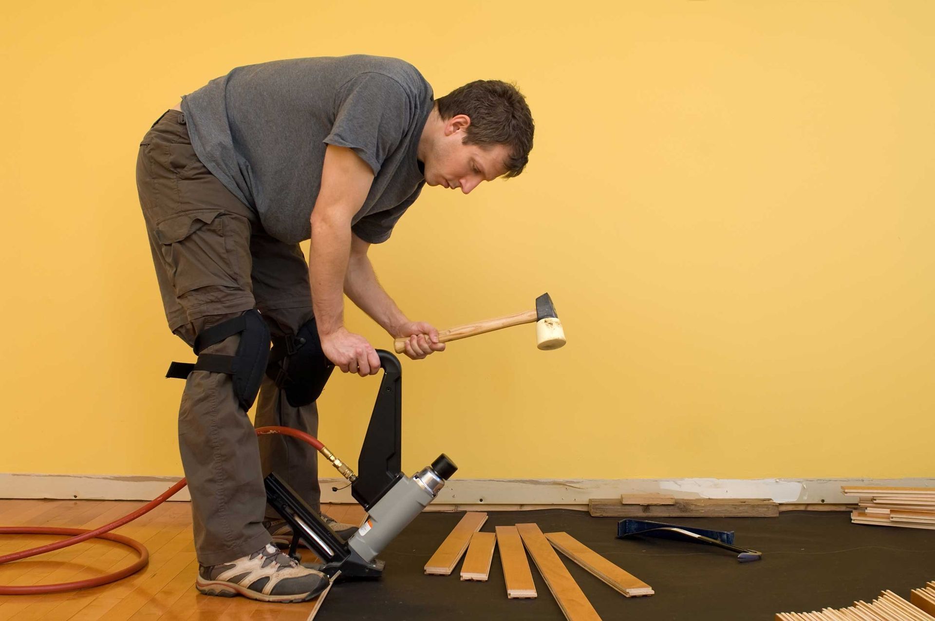 Technician using a mallet and floor nailer for a hardwood flooring installation project.