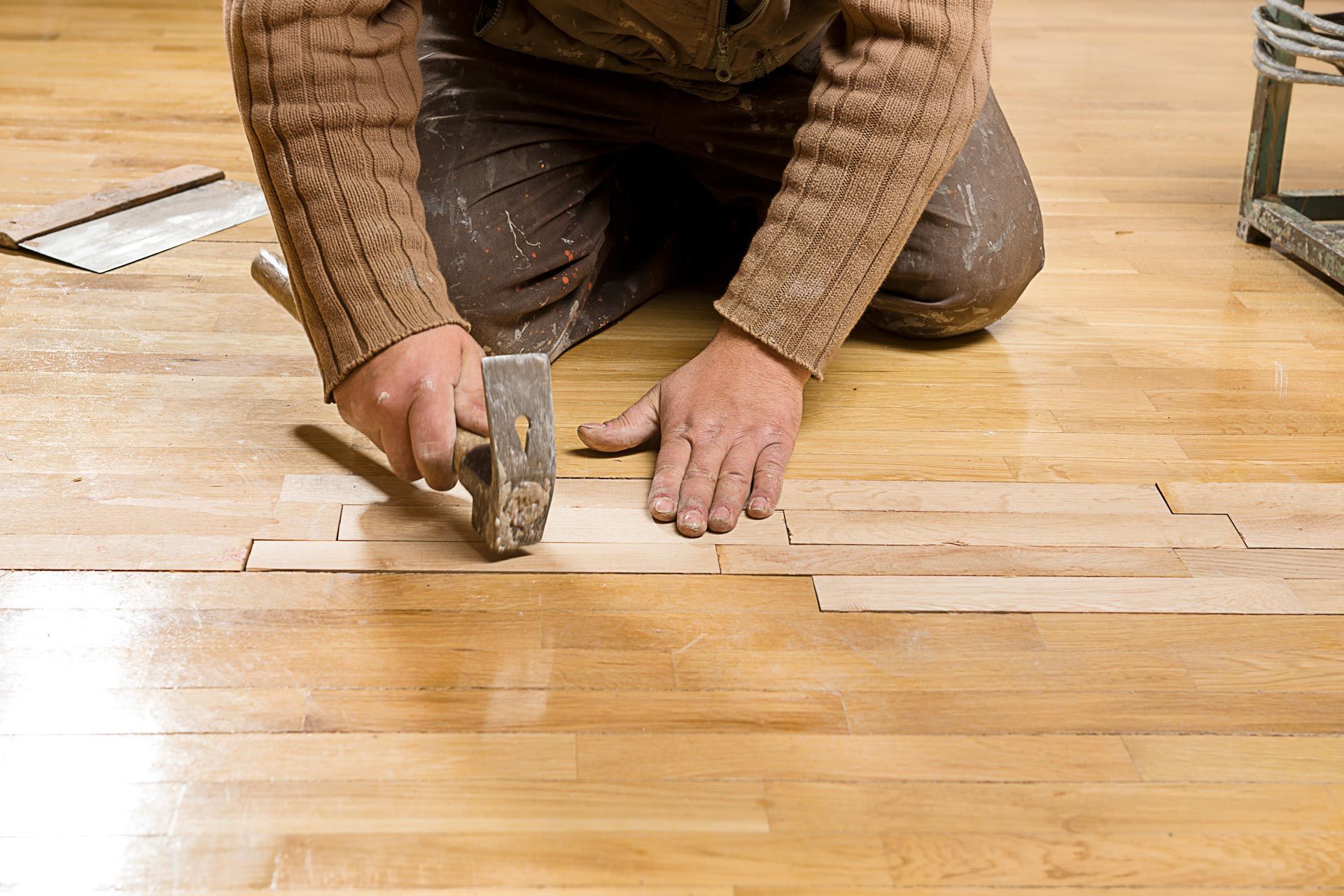A worker kneels, repairing hardwood floorboards with a hammer.
