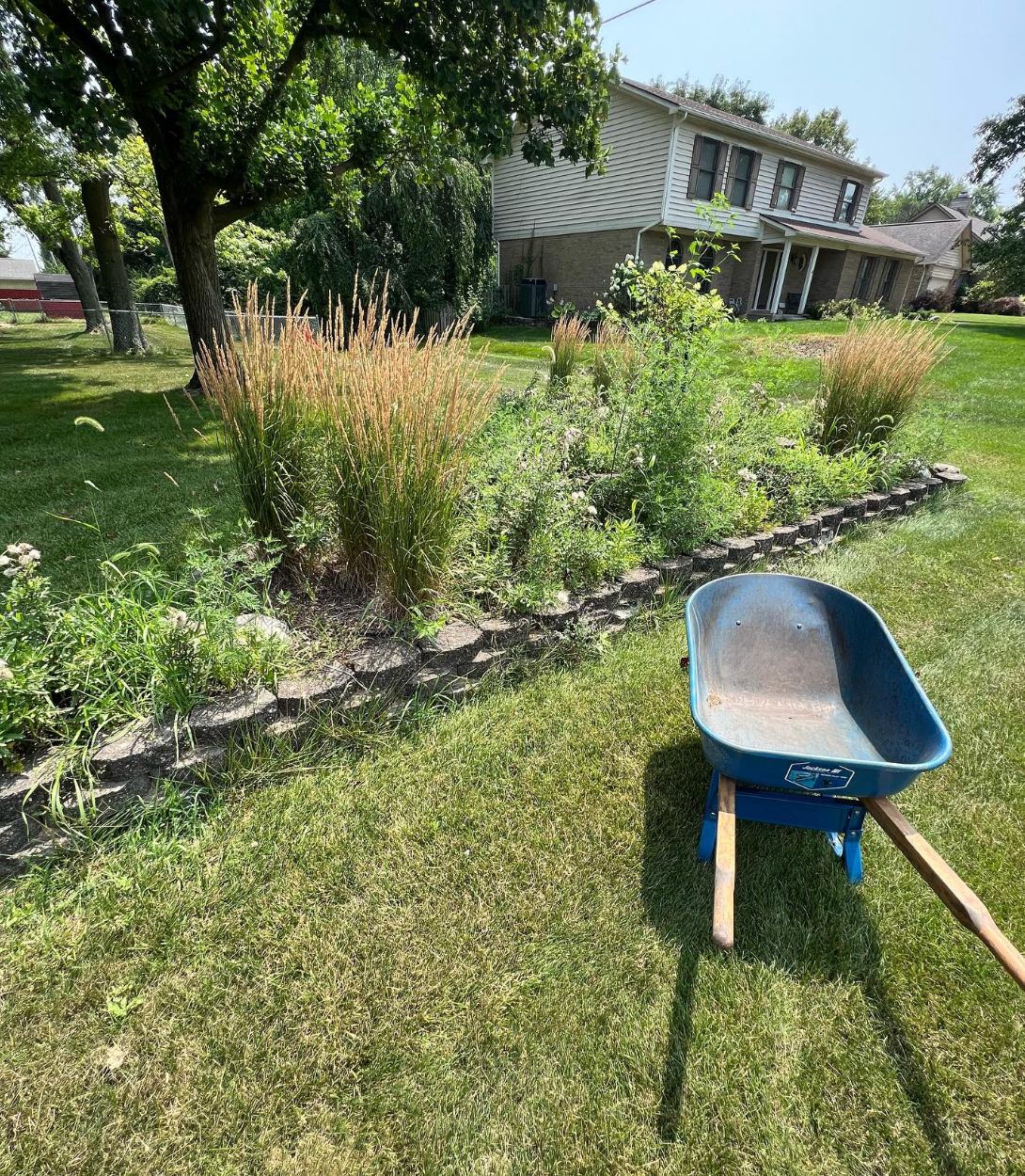 A wheelbarrow is sitting in the grass in front of a house.