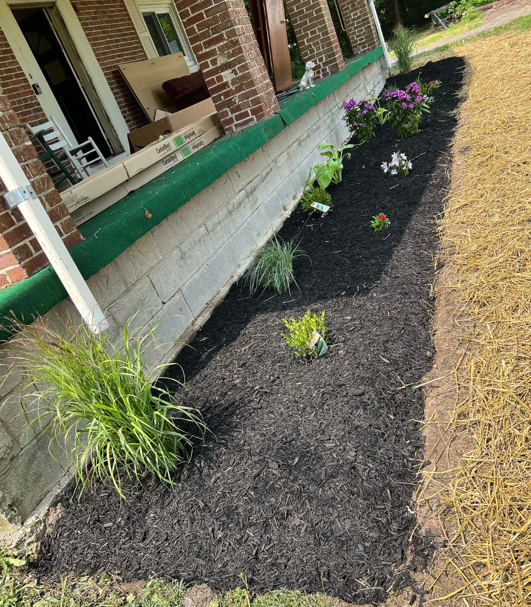 A brick house with a porch and a garden in front of it.