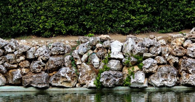 A stone wall surrounding a body of water with trees in the background.