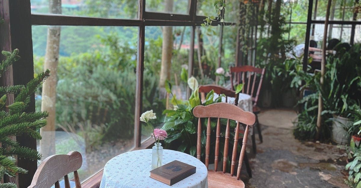 A table and chairs in a greenhouse with a book on it.