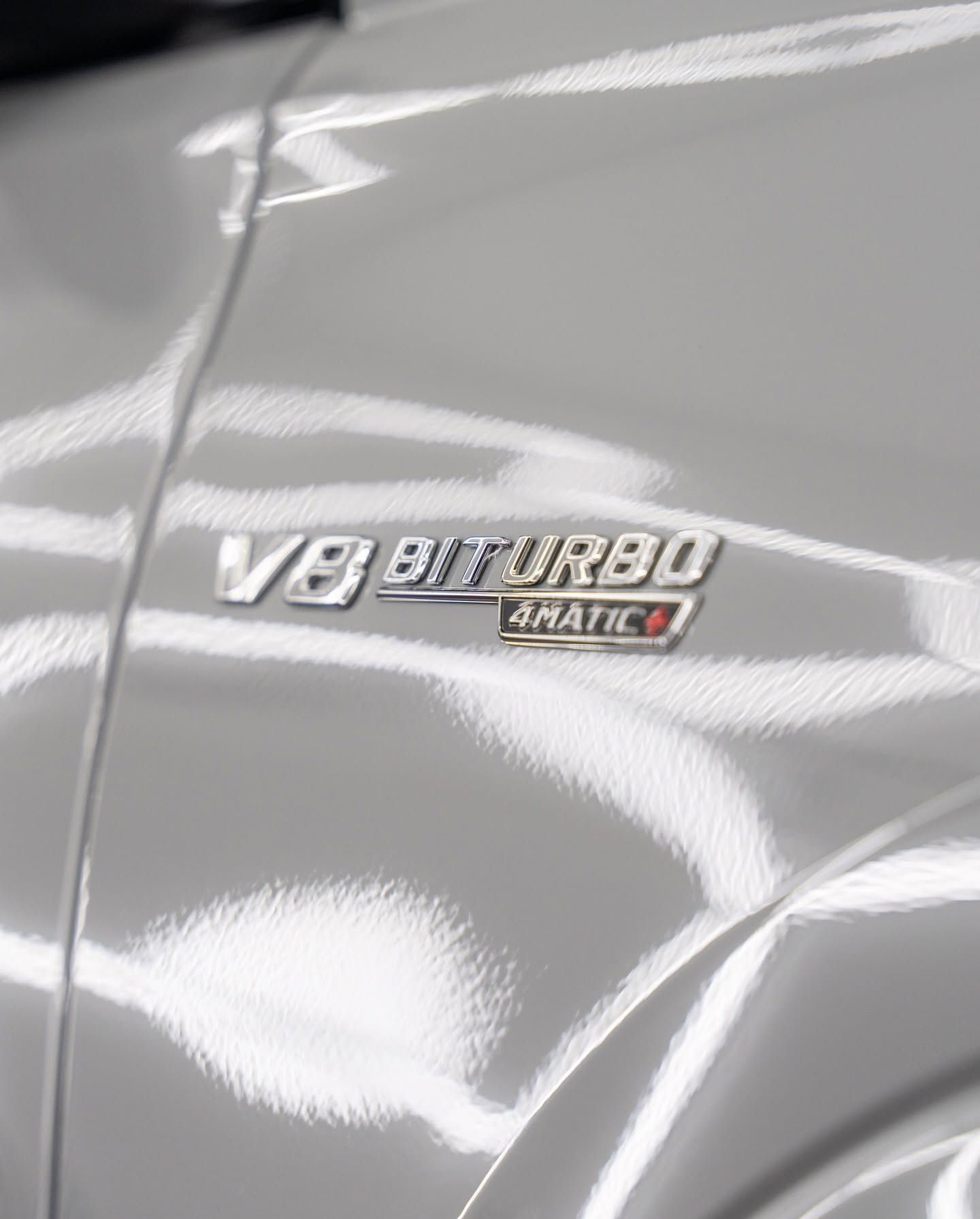 Close-up of a silver car badge reading “V8 biturbo 4matic” on a glossy body panel