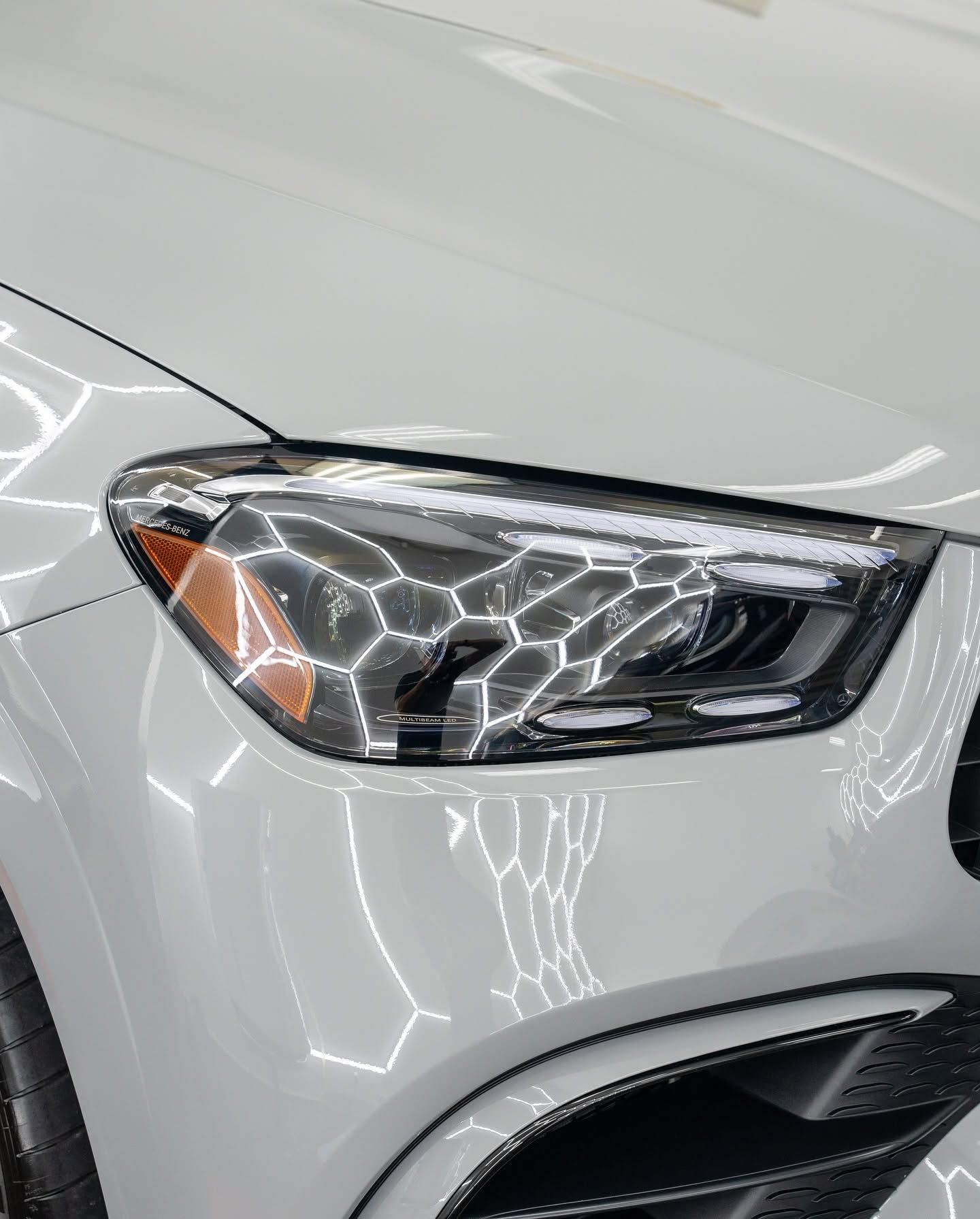 Close-up of a white car’s front headlight and bumper with reflections on the glossy surface