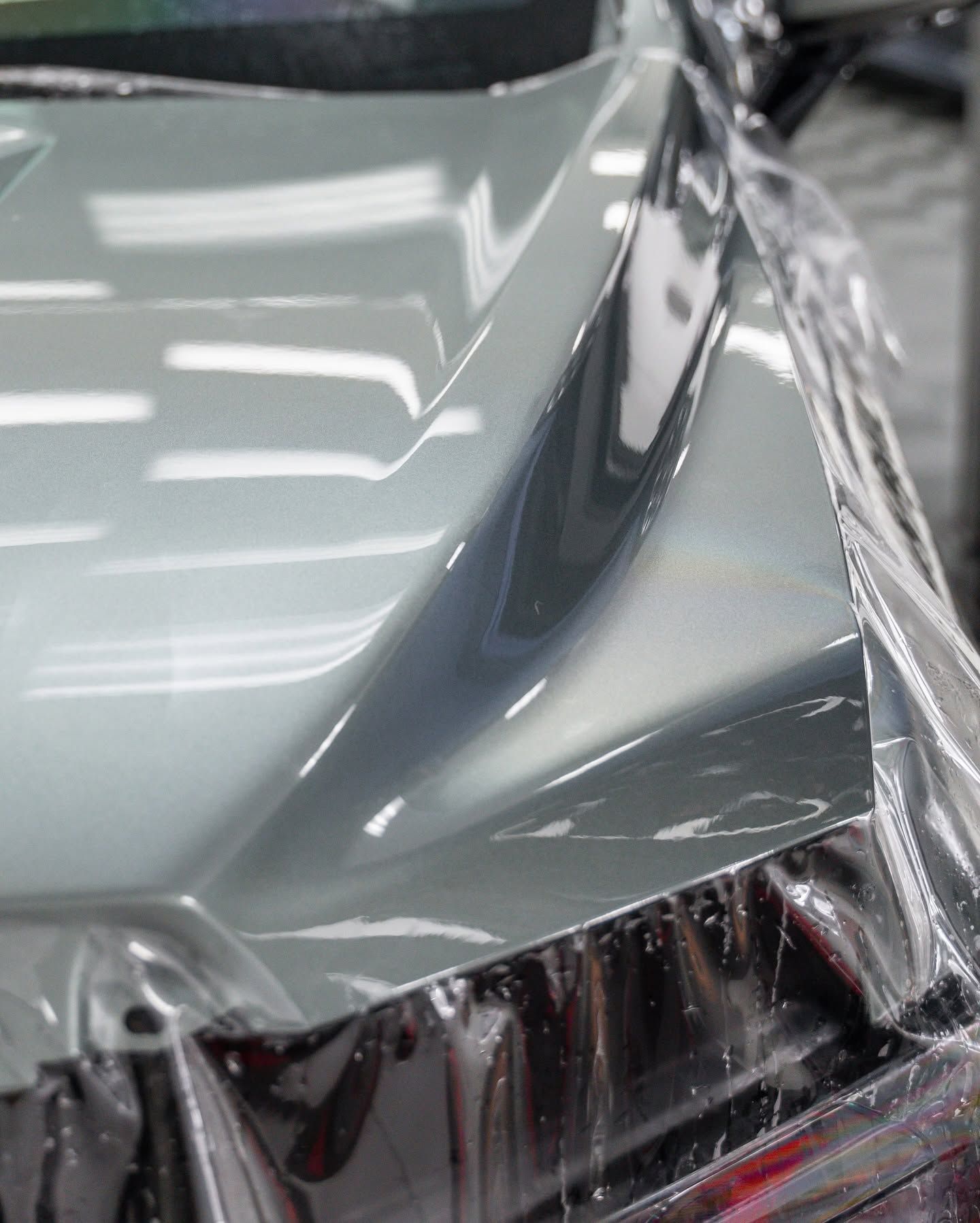 Close-up of a silver car hood and headlight covered in protective plastic wrap