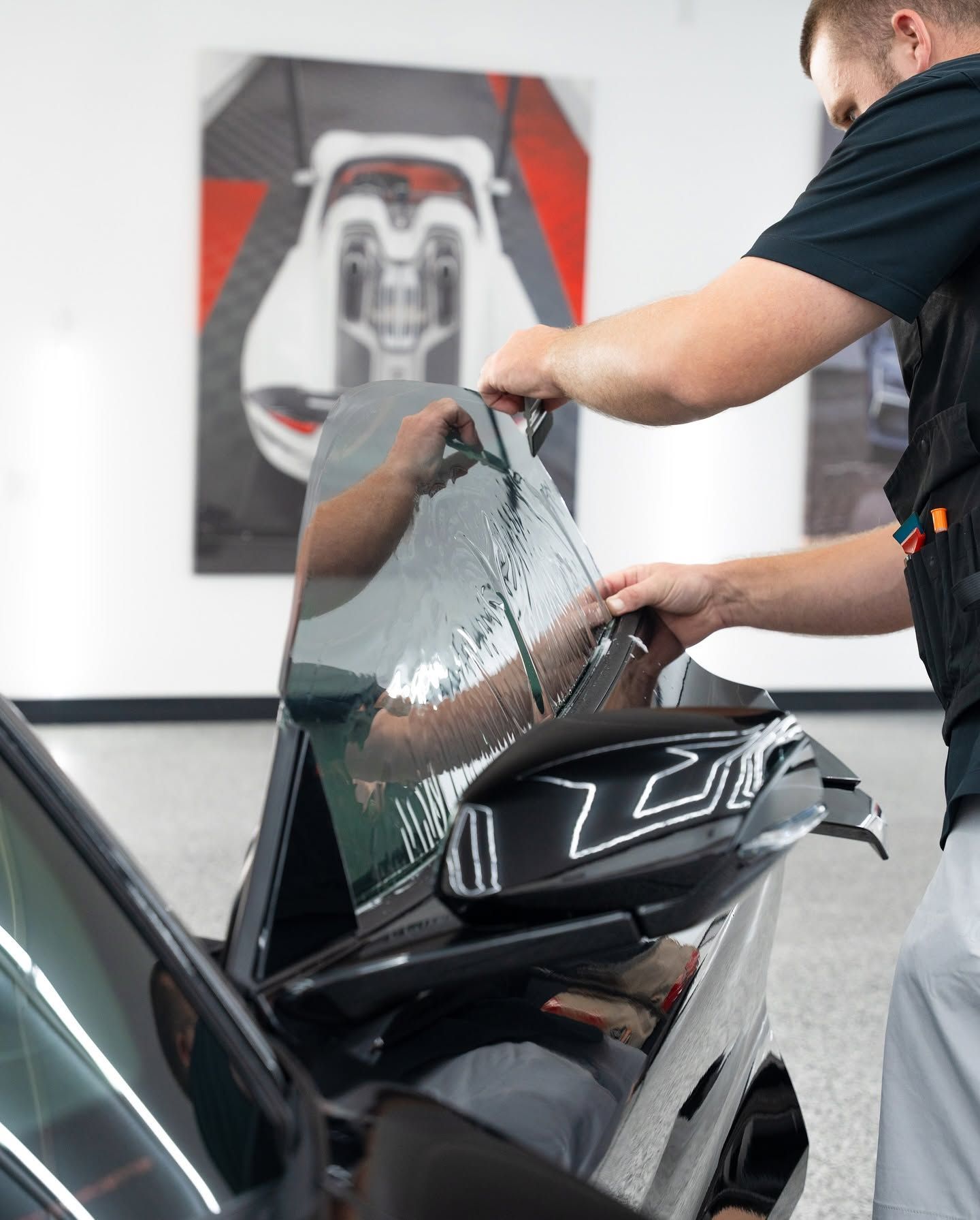 Technician applying clear protective film to a black car door in a workshop