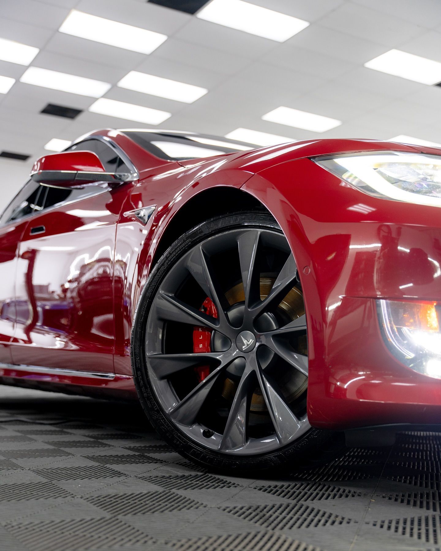 Red Tesla car, front view, in a showroom, with a glossy finish.