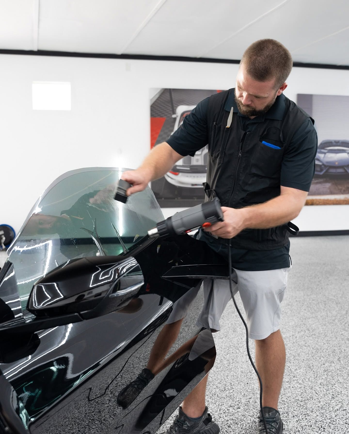 Man cleaning a black motorcycle windshield indoors with a cloth and spray bottle