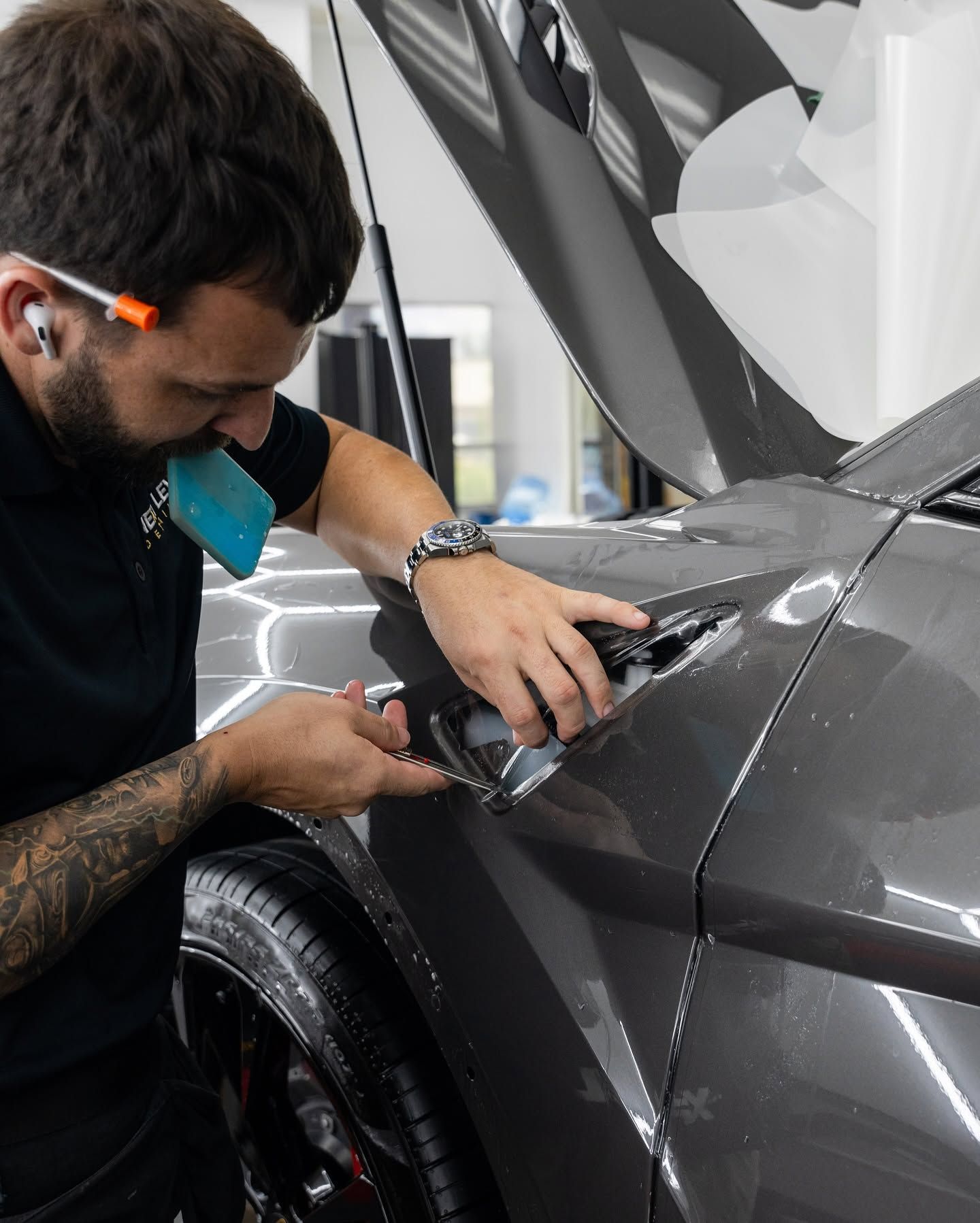 Technician installing film on a gray sports car’s headlight in a workshop