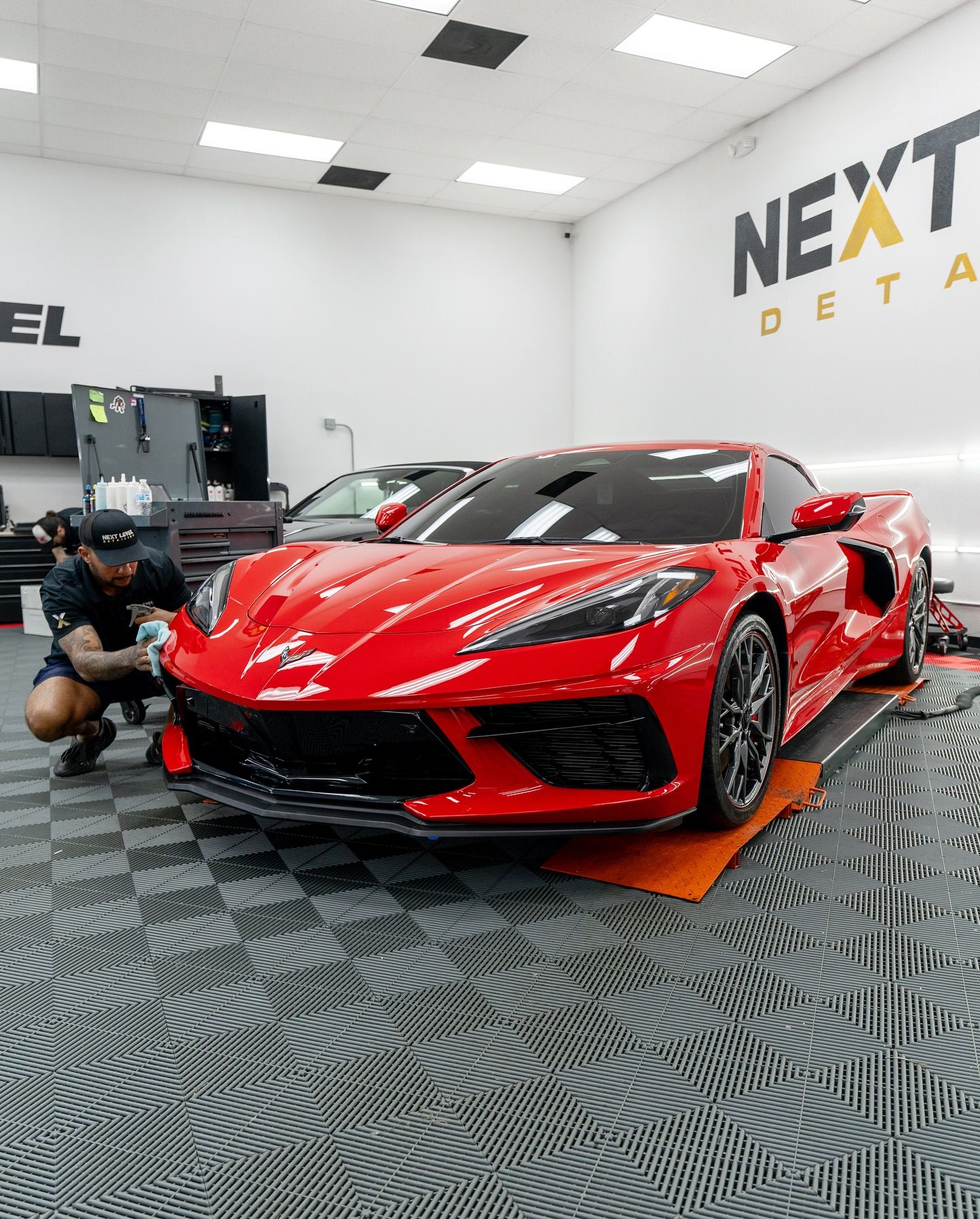 A red sports car being detailed in a shop with a person kneeling near the front. 