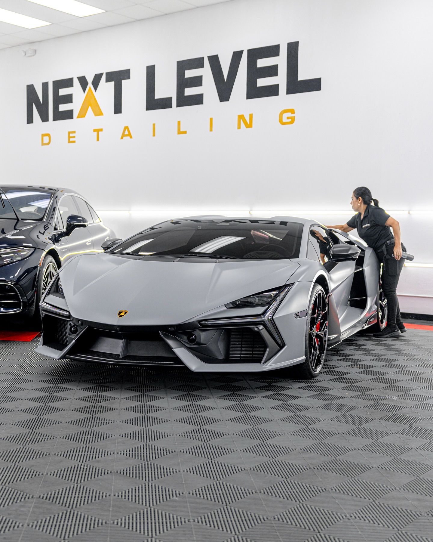 A man is kneeling down next to a white car in a garage.