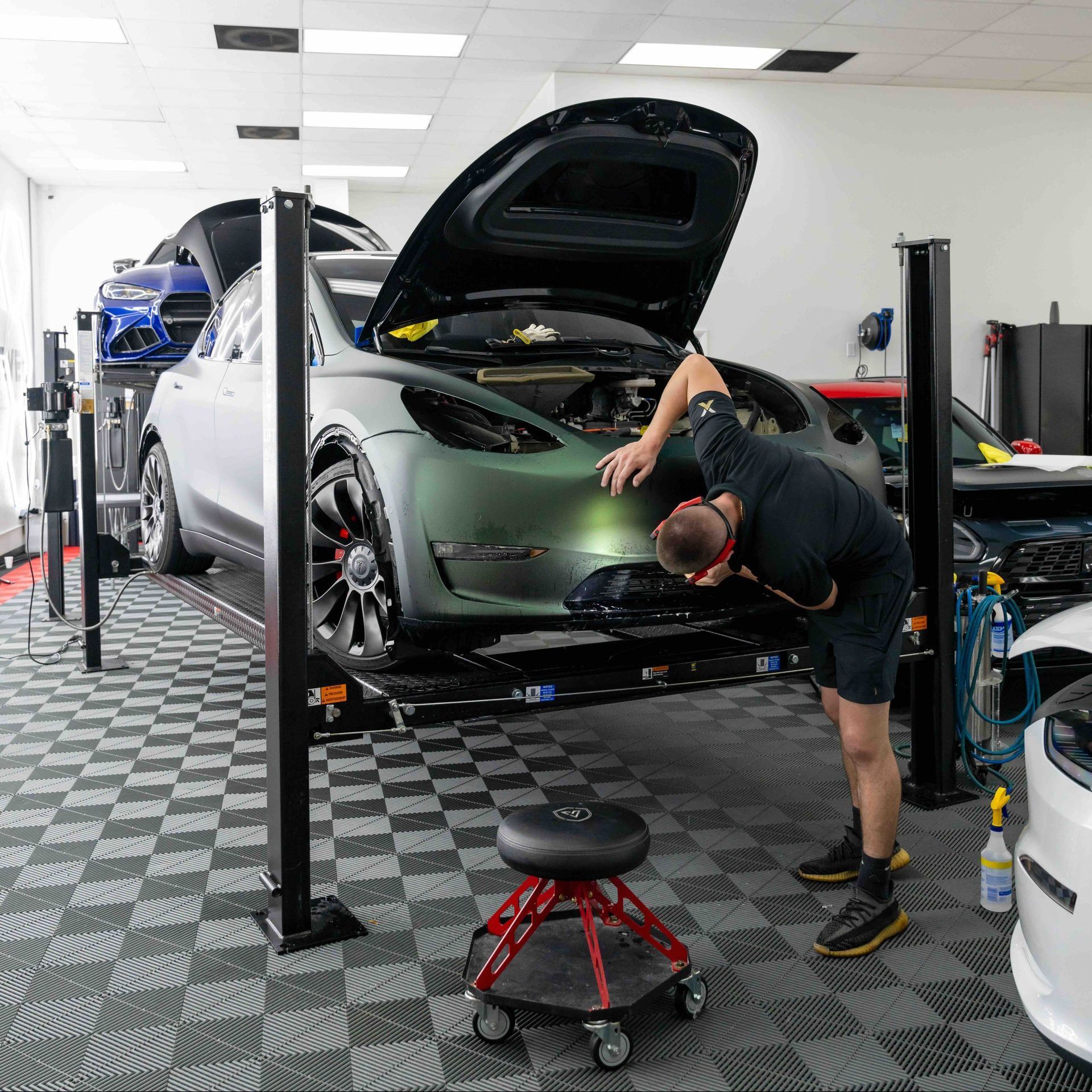 A man is working on a car in a garage with the hood up.