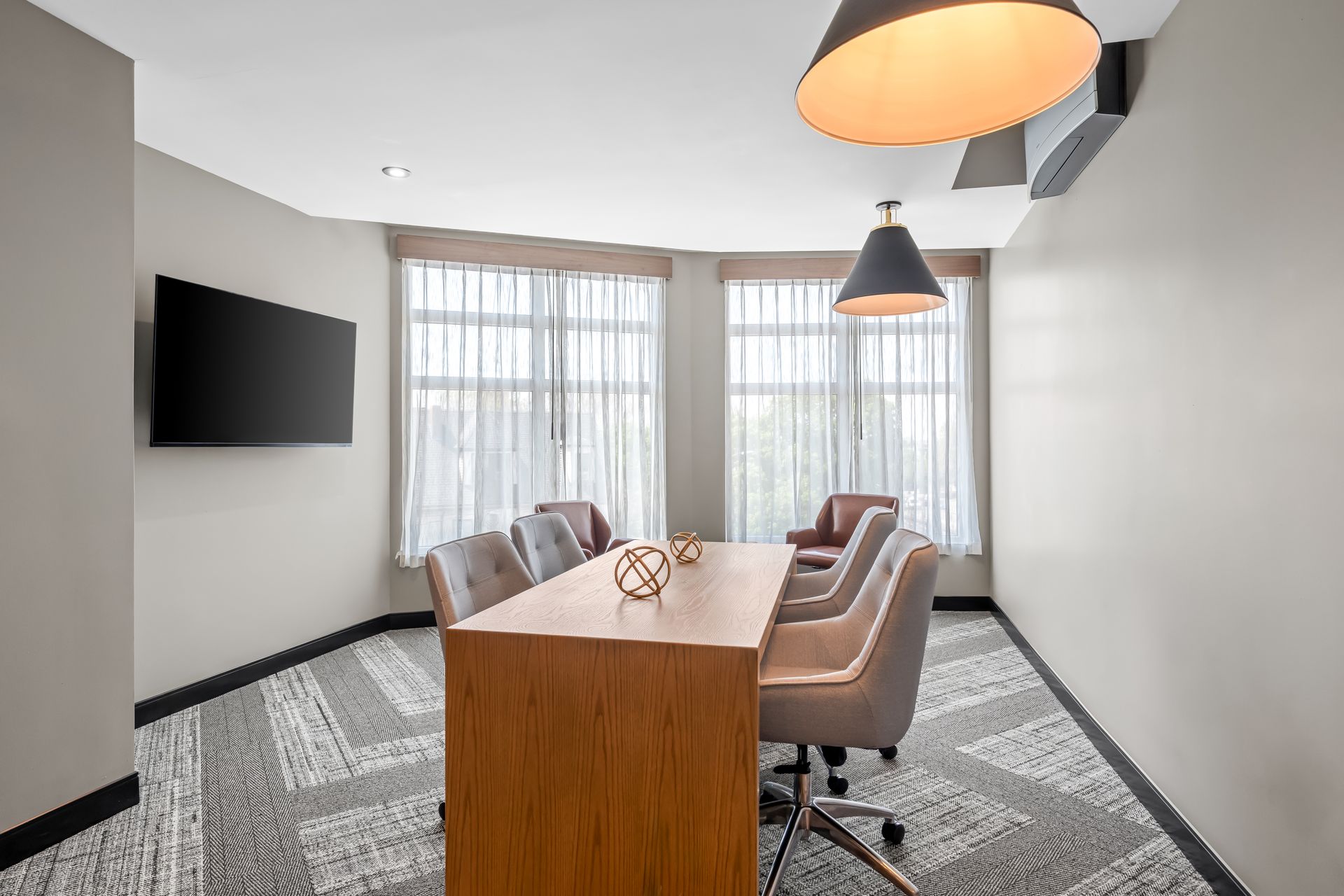 Modern conference room with wooden table, gray chairs, wall-mounted TV, and large windows