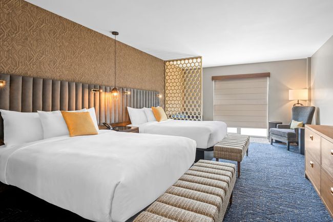 Hotel room with two beds, TV, desk, patterned wallpaper, and sheer curtains.