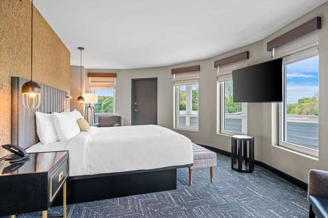 Bedroom with gray upholstered bed, patterned gold wall, two windows, and a chaise lounge.