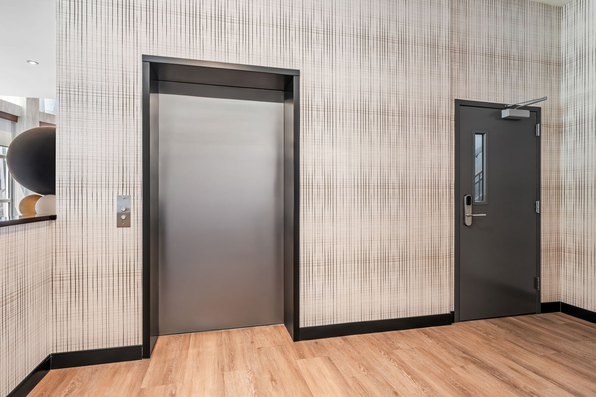 Office hallway with an elevator beside a dark door and wood floor