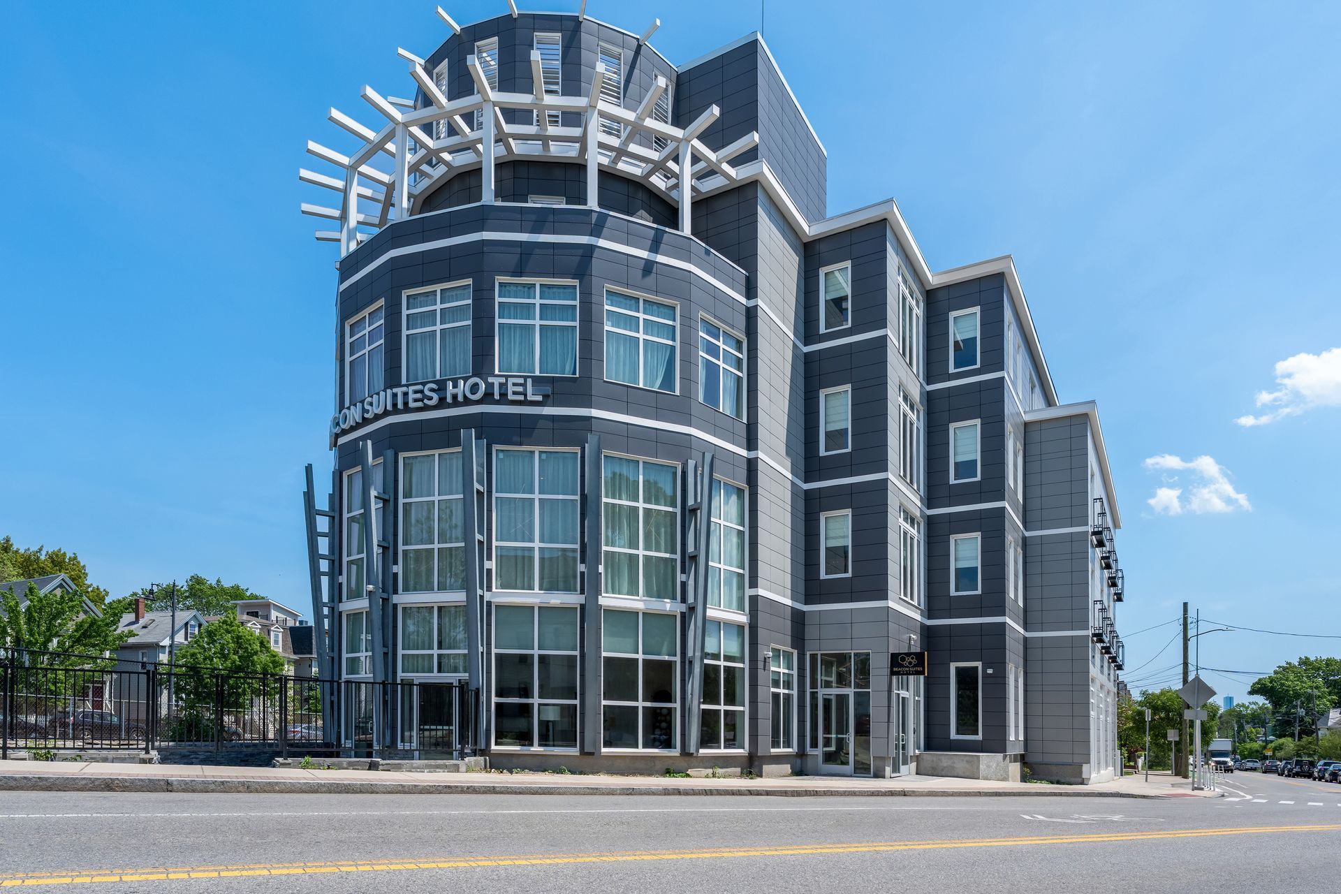 Modern glass-front hotel building on a sunny street corner under a blue sky