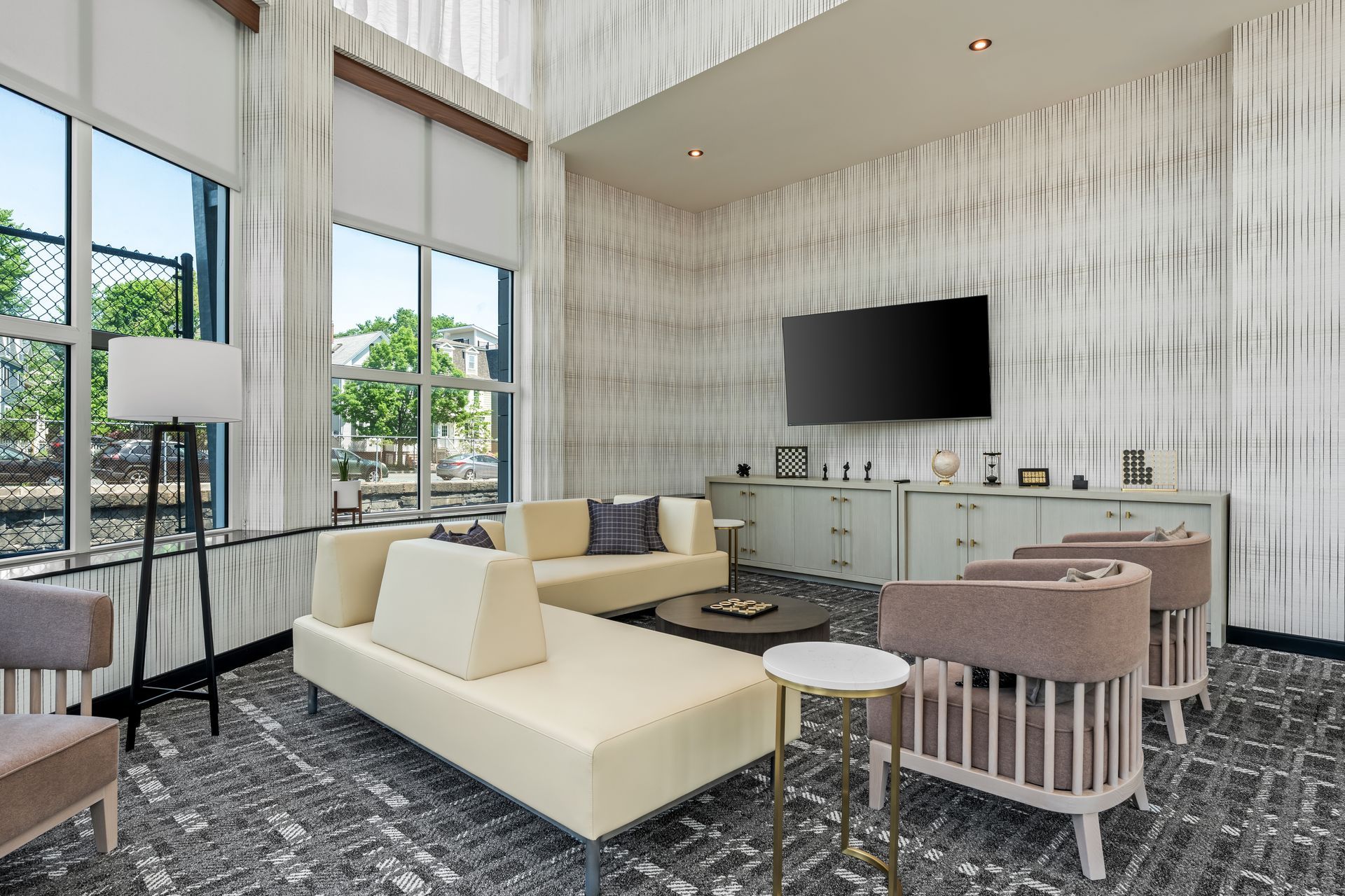 Modern living room with large windows, cream sectional, TV, and chairs on a patterned rug