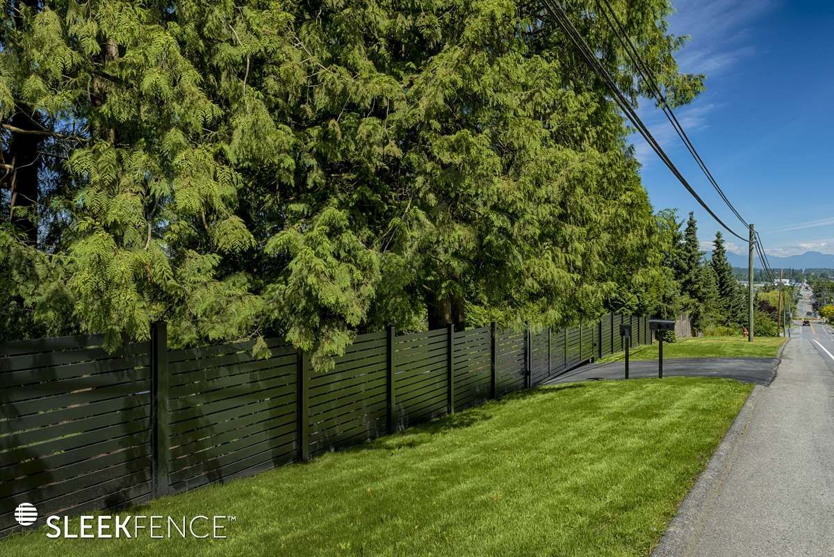 A fence surrounds a lush green field next to a road.