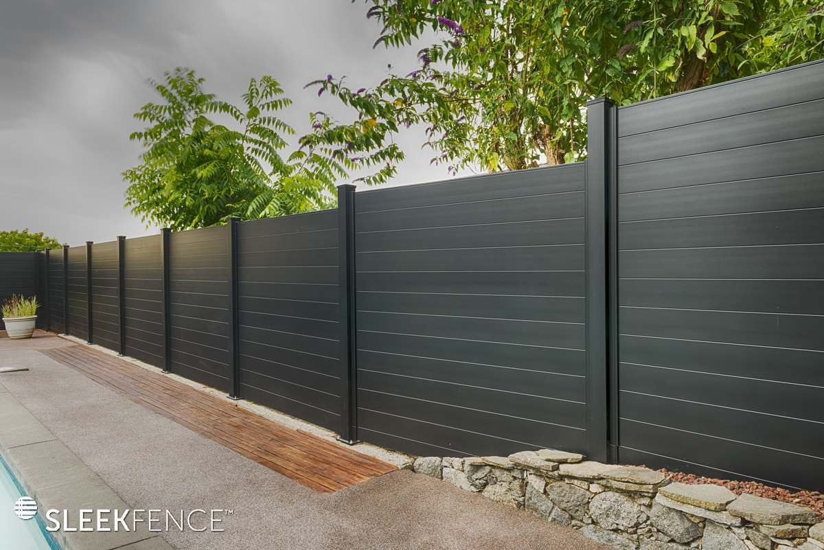 A black fence is surrounded by trees and a stone wall.