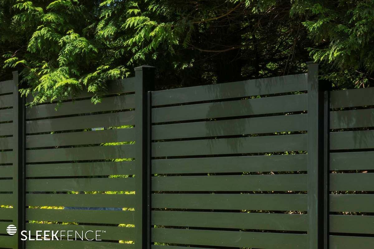 A green wooden fence with trees in the background