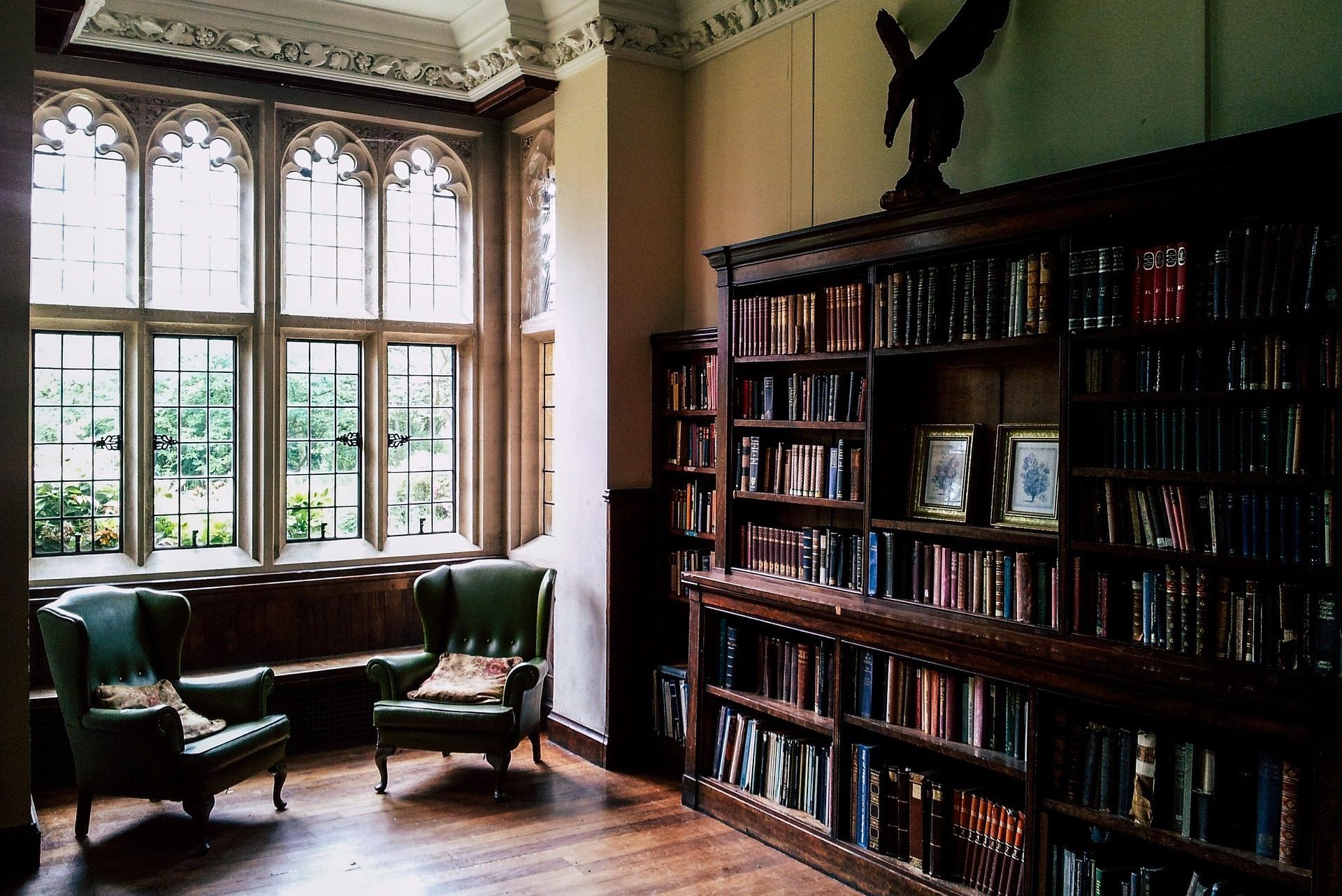 Elegante sala de biblioteca con sillones de cuero verde, estanterías altas y grandes ventanales en arco