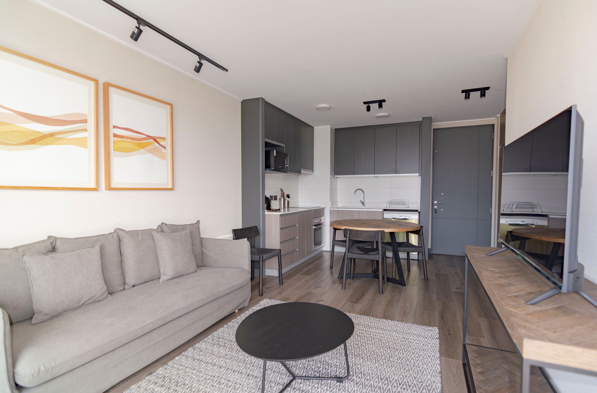 Luminoso y moderno salón con sofá gris, mesa de centro redonda, cuadros en la pared y cocina abierta
