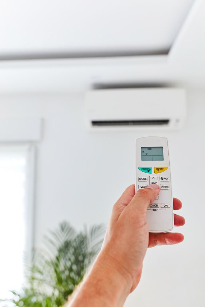Modern Air Conditioner Unit With A Hand Holding A Remote — Oriel Refrigeration and Air Conditioning in Narromine, NSW