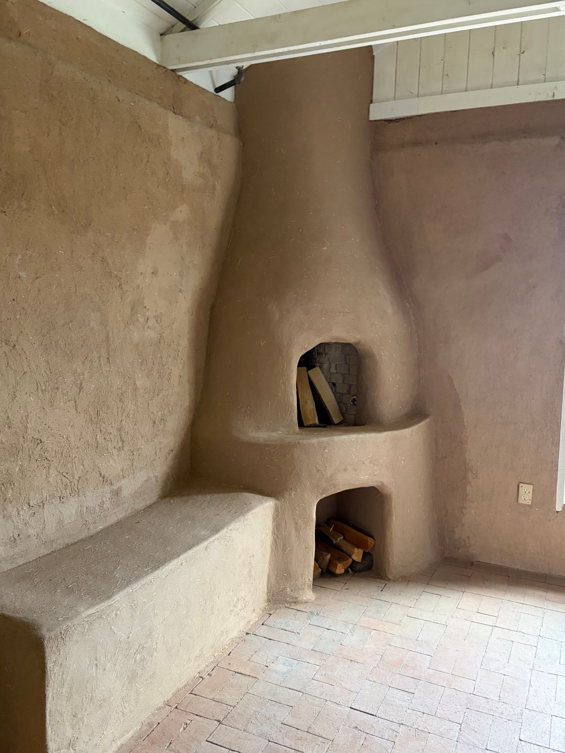 An old adobe fireplace with white plaster peeling off and large holes in the mud