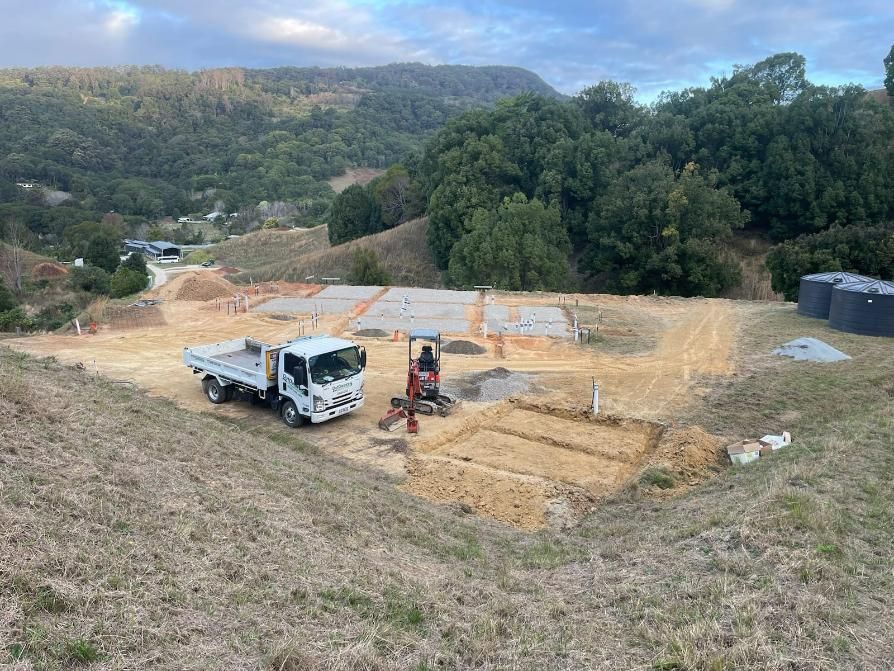 A White Truck Is Parked in A Dirt Field Next to A Small Excavator — Kontek Constructions in Jimboomba, QLD