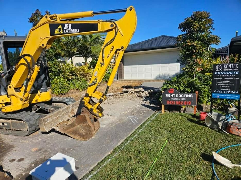 A Yellow Excavator Is Working on A Driveway in Front of A House — Kontek Constructions in Jimboomba, QLD