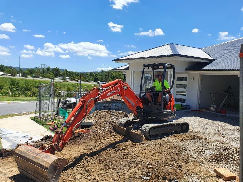 A Man is Driving an Excavator in Front of a House — Kontek Constructions in Jimboomba, QLD