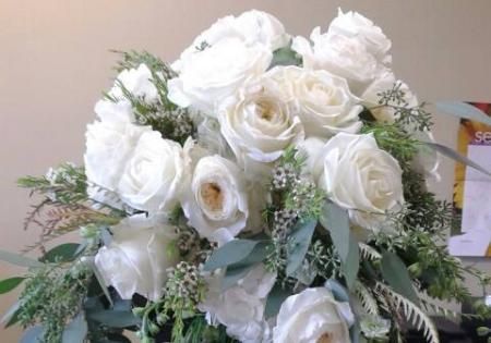 White rose bouquet with greenery and a pale blue ribbon on a table