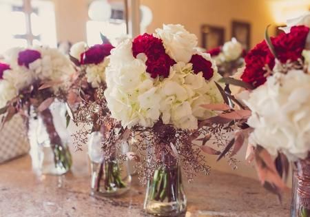 Glass vases of white and burgundy flowers arranged on a banquet table